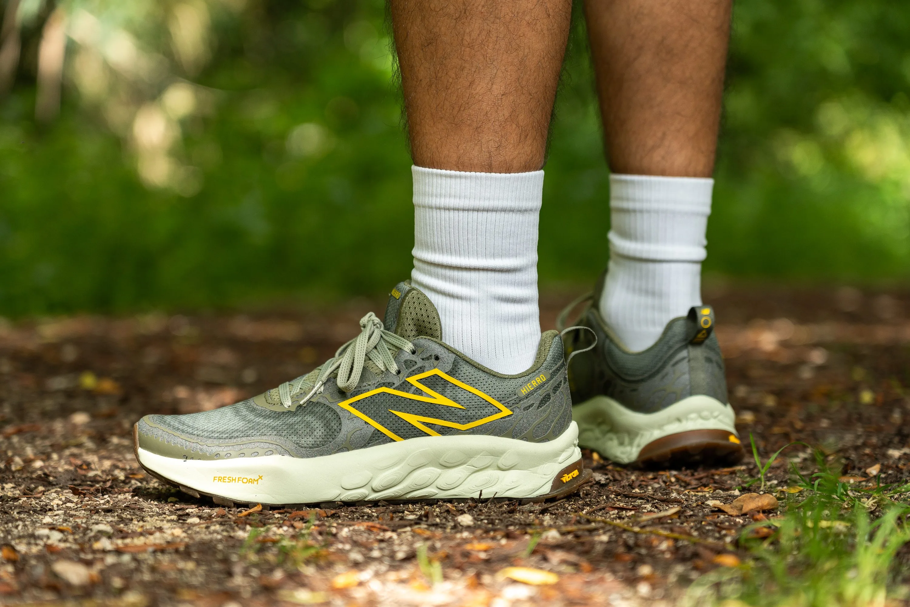 A New Balance Hierro trail running shoe on a forest singletrack, showing a cushioned midsole and rugged outsole
