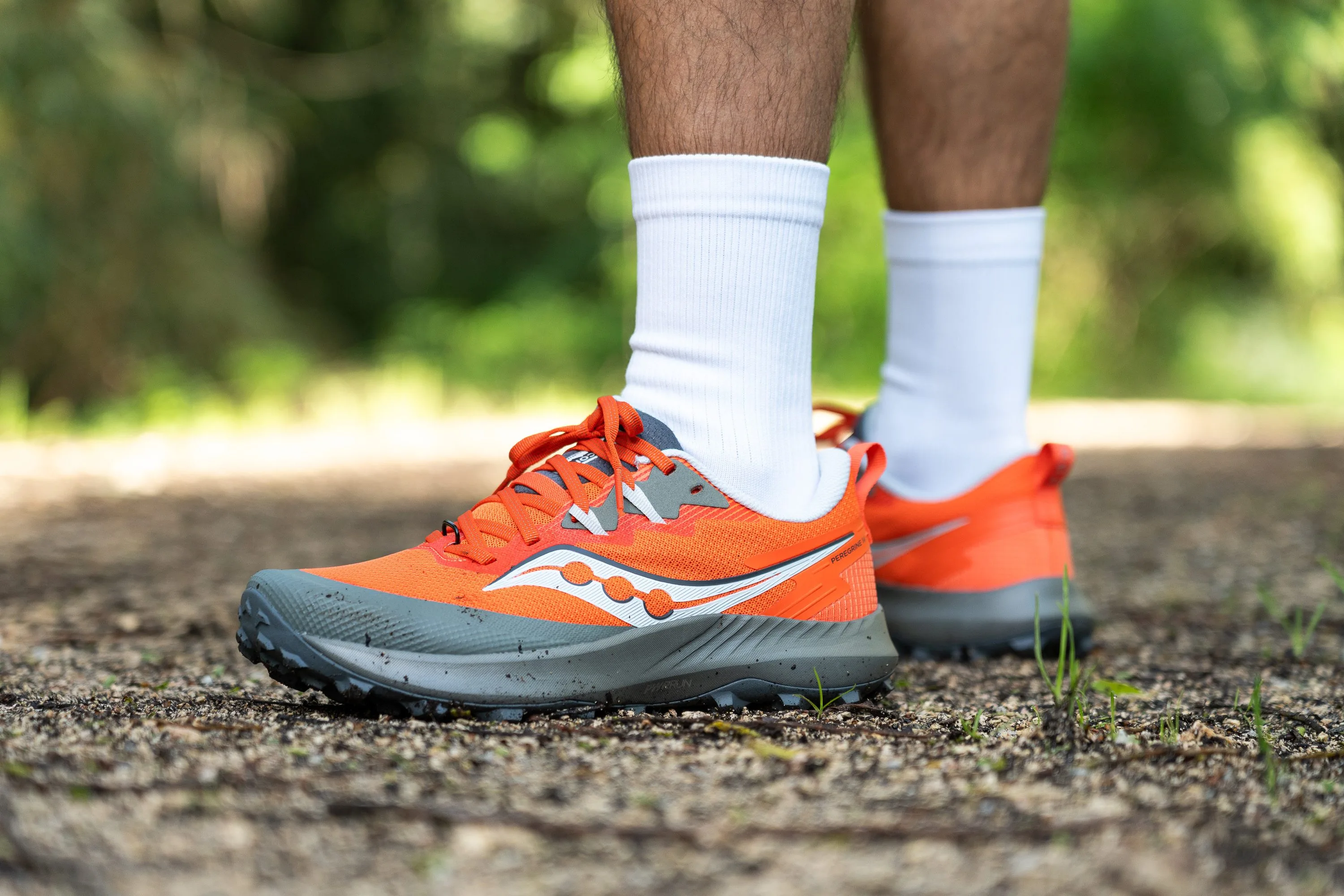 A Saucony Peregrine trail running shoe on muddy ground, showing aggressive lugs designed for traction