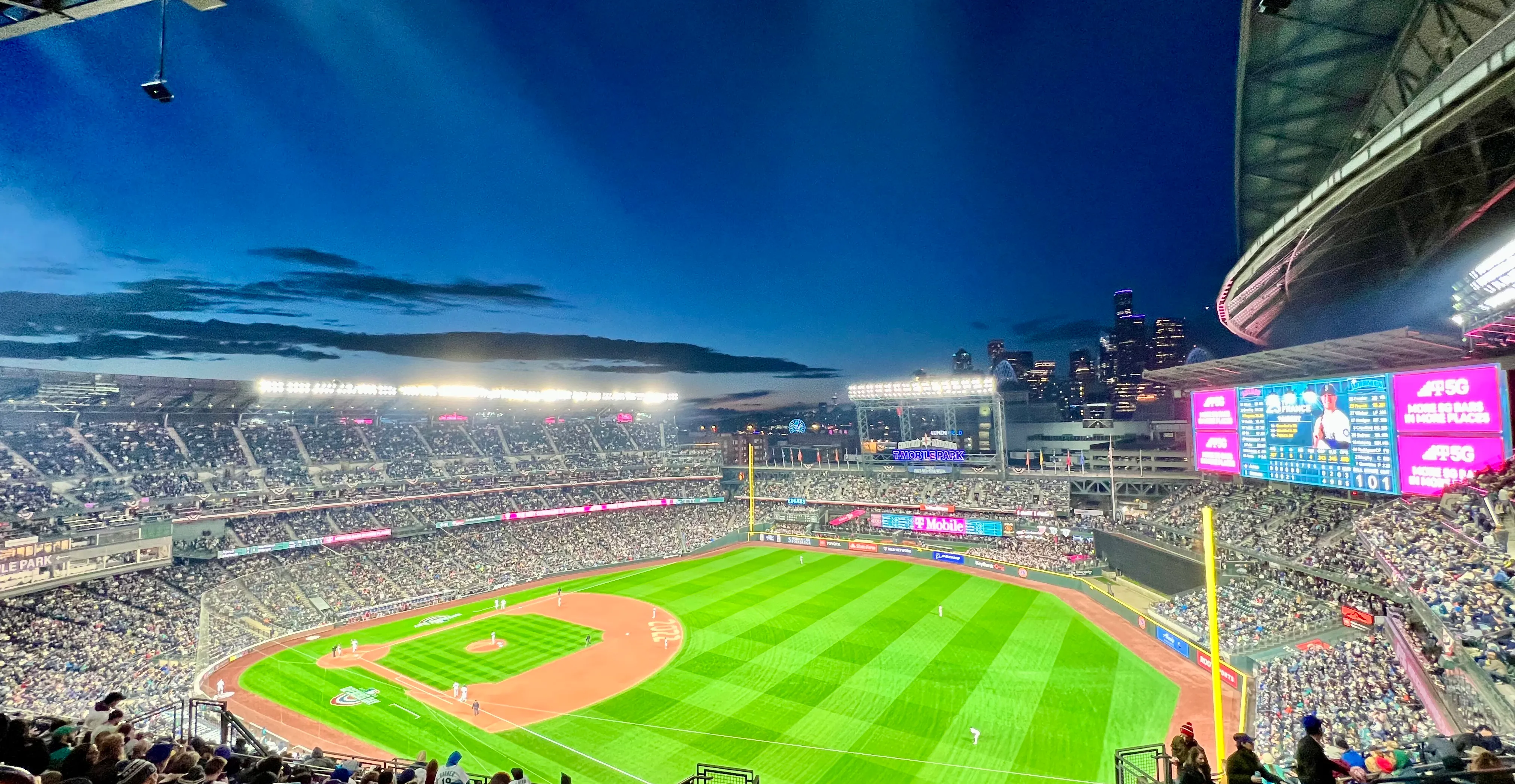A baseball stadium scoreboard glowing at night with fans in the stands, visually matching the idea of constant score checking