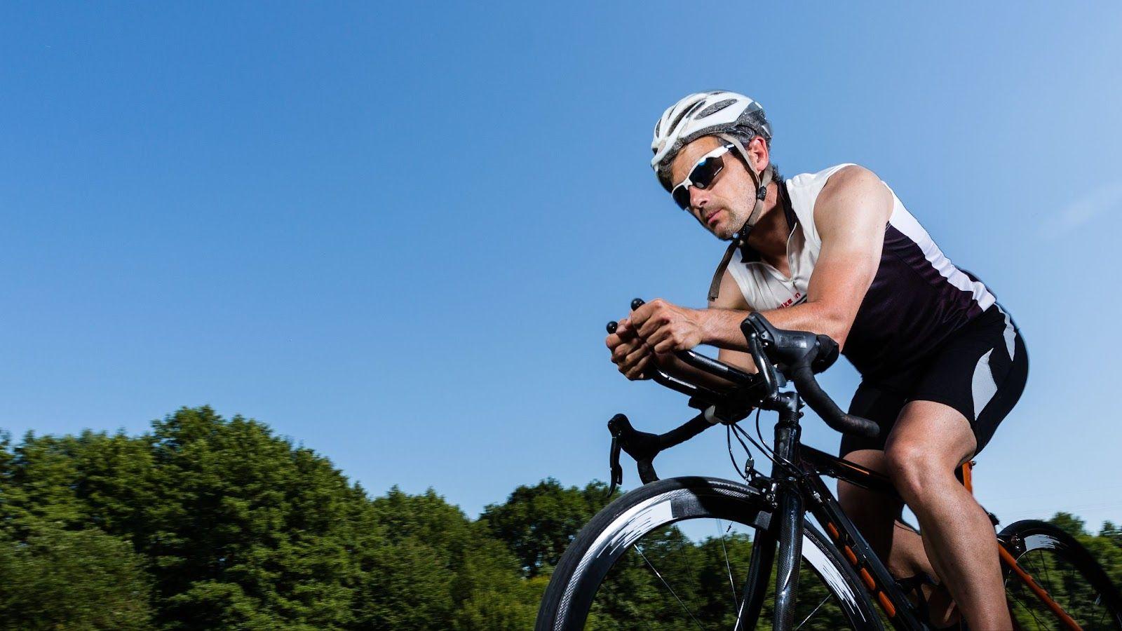 A beginner triathlete riding a road bike on a quiet suburban road during training, wearing a helmet and cycling kit