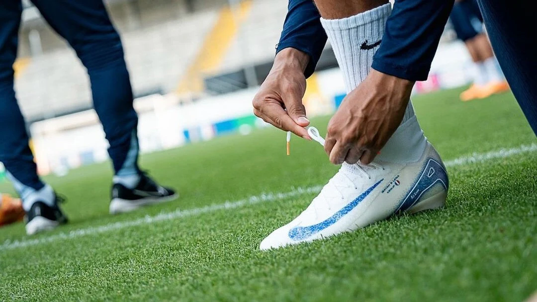 A close view of molded firm ground soccer cleats digging into natural grass during a match as a player changes direction