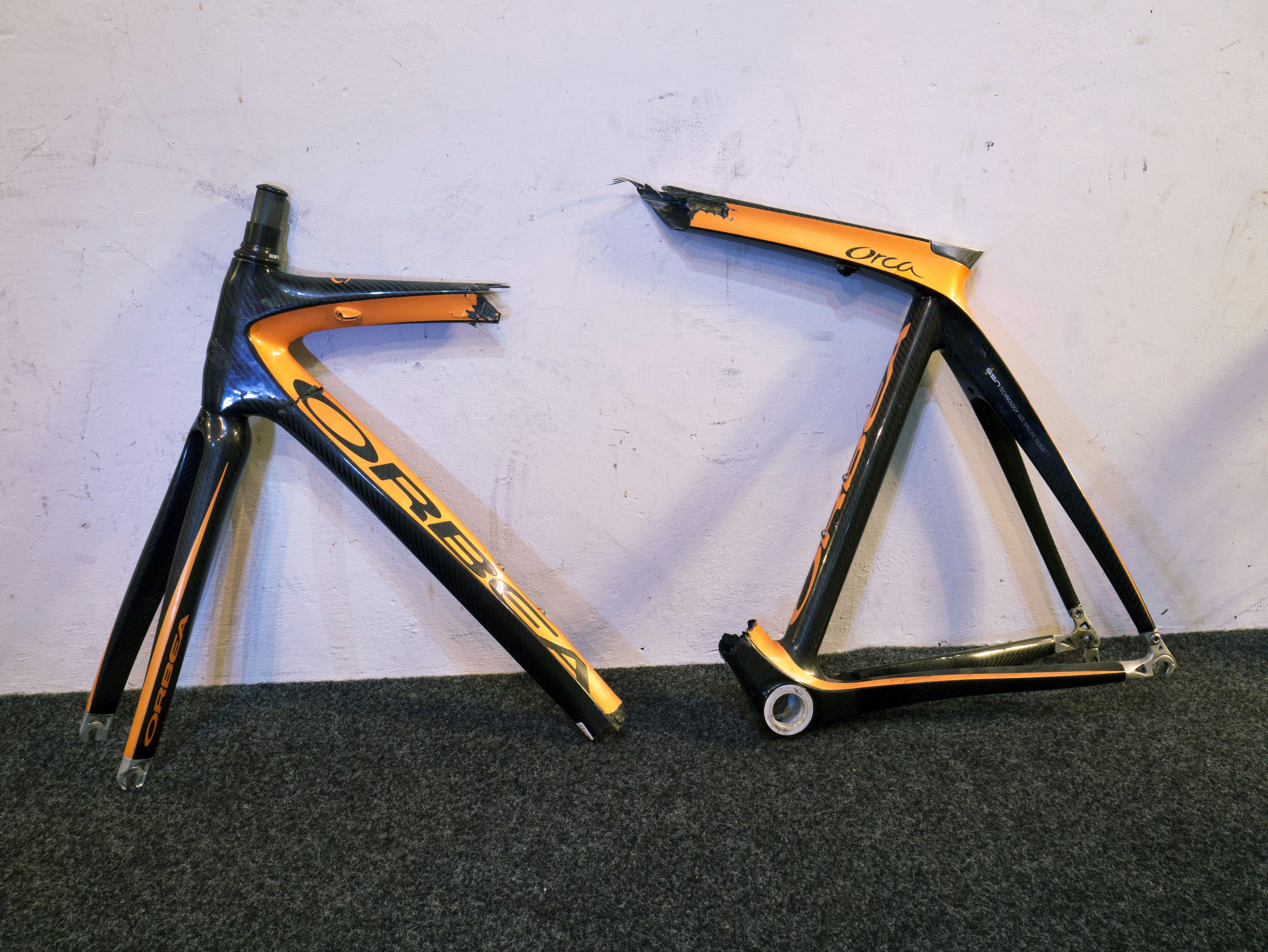 A cyclist in a garage closely inspecting a road bike frame near the bottom bracket area after a minor crash
