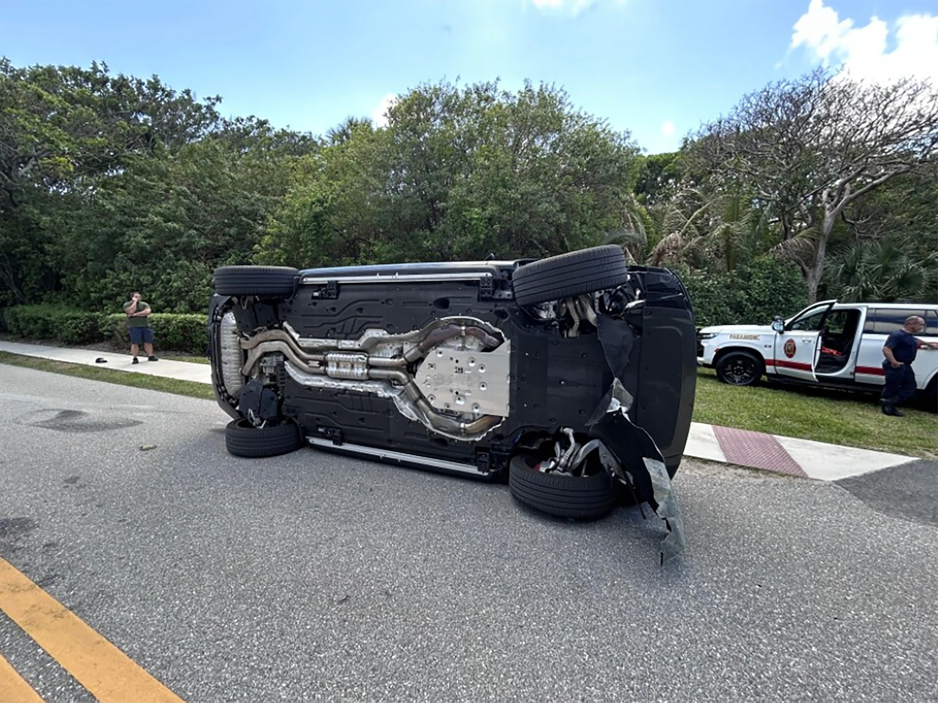 A damaged SUV resting on its side on a Florida roadway while police officers secure the scene near another vehicle, news photography style