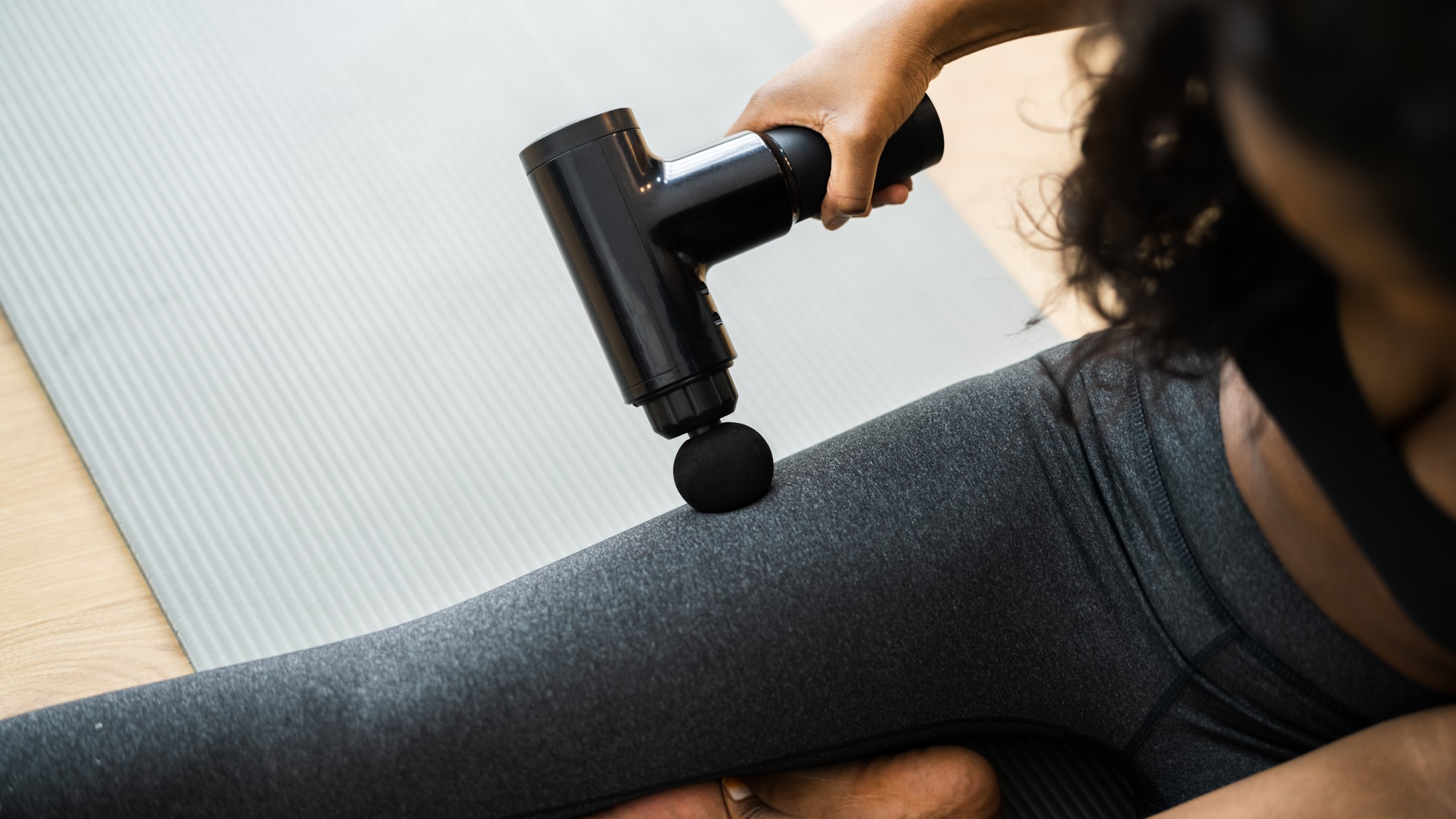 A distance runner near a major marathon staging area using a massage gun on the calf while other runners warm up nearby