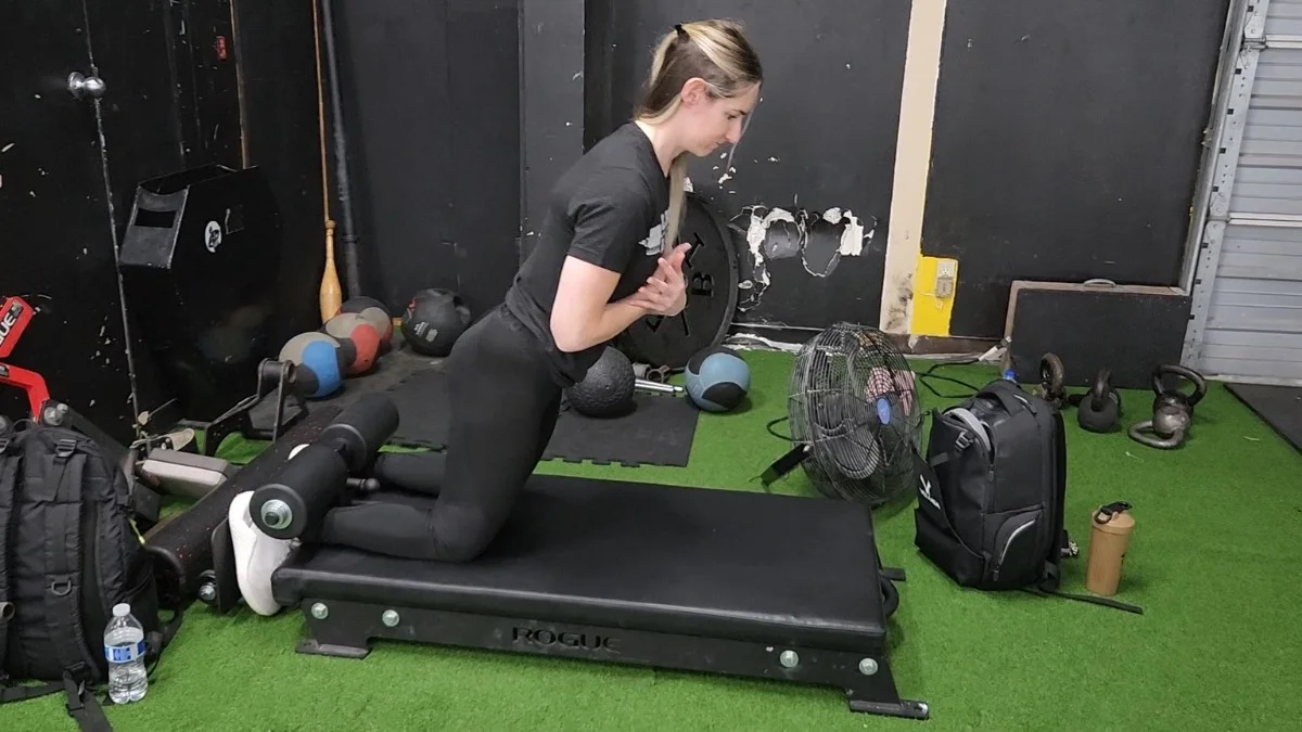 A field sport athlete kneeling on a mat performing a Nordic hamstring curl while a partner holds their ankles in a training facility