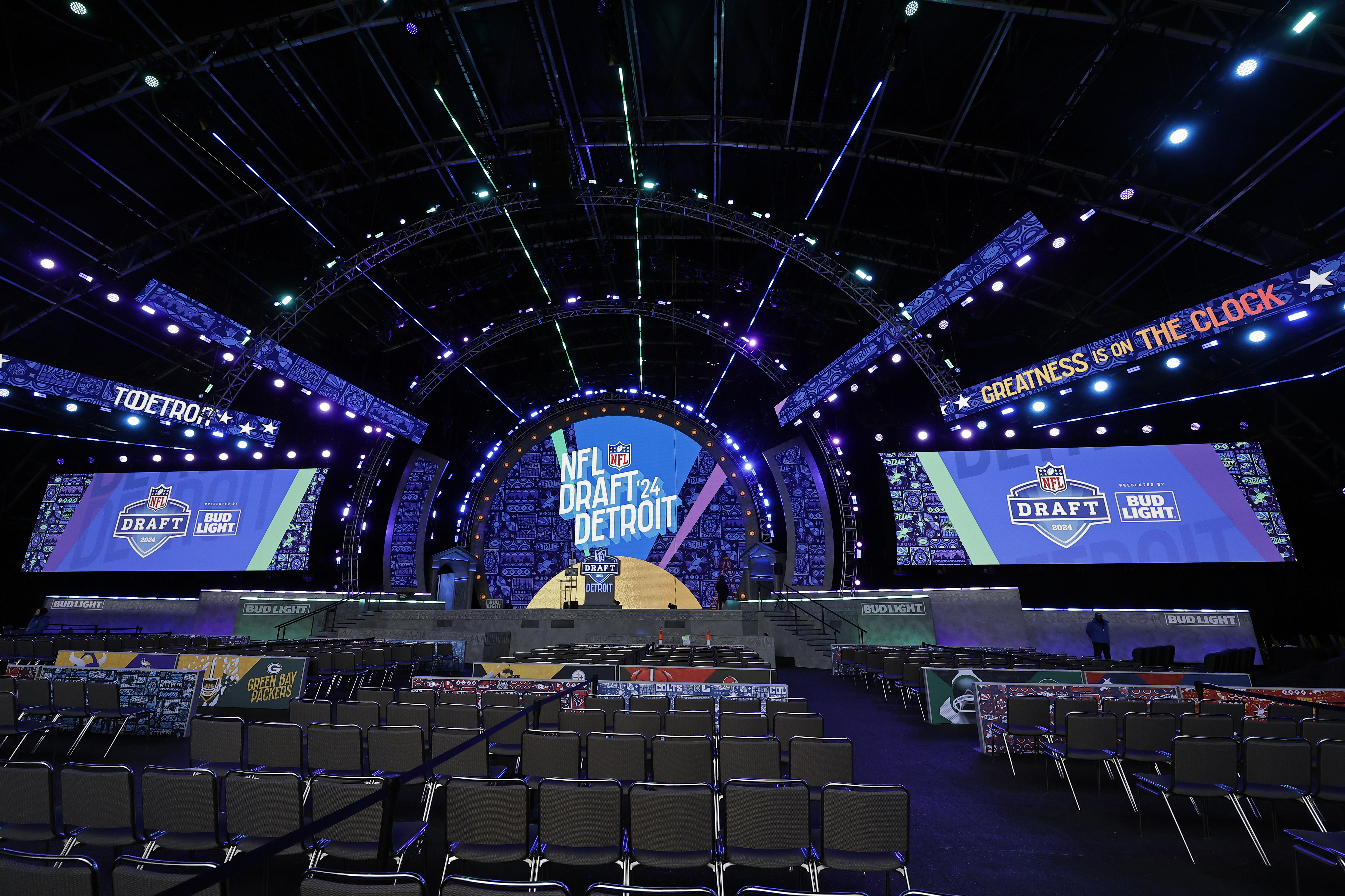 A first-round NFL Draft prospect walking toward the stage holding a team jersey while fans and photographers watch from the floor