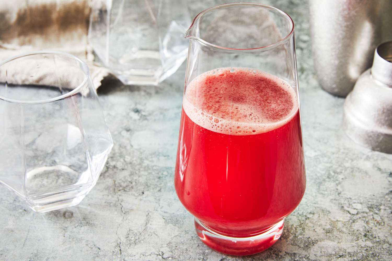 A glass of fresh watermelon juice on a kitchen counter with cut watermelon wedges nearby