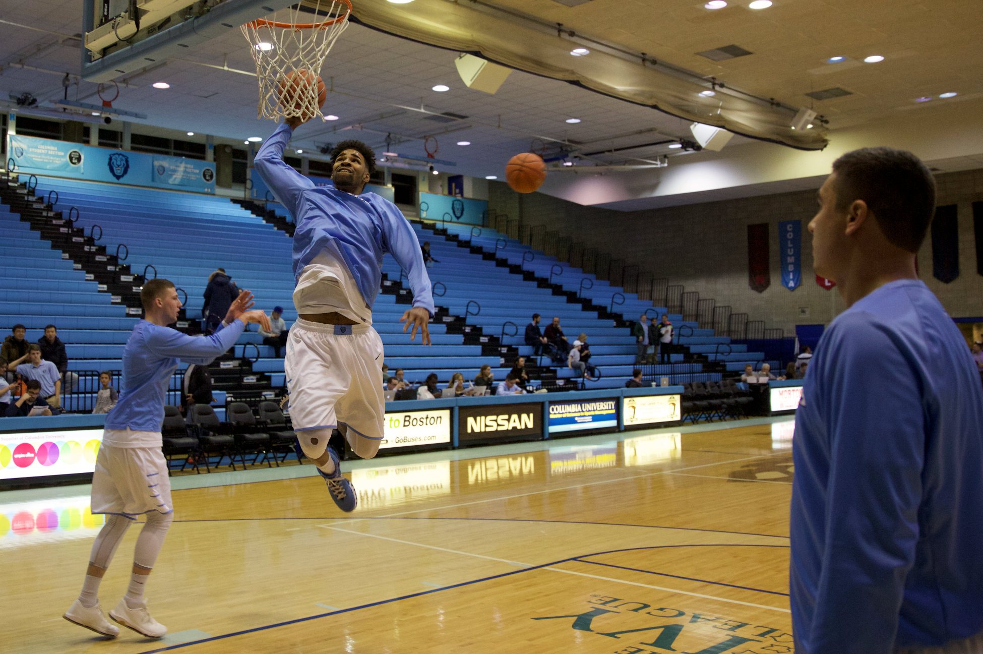 A high school basketball team running pregame layup lines on a bright gym court, players in motion with a coach watching from the sideline