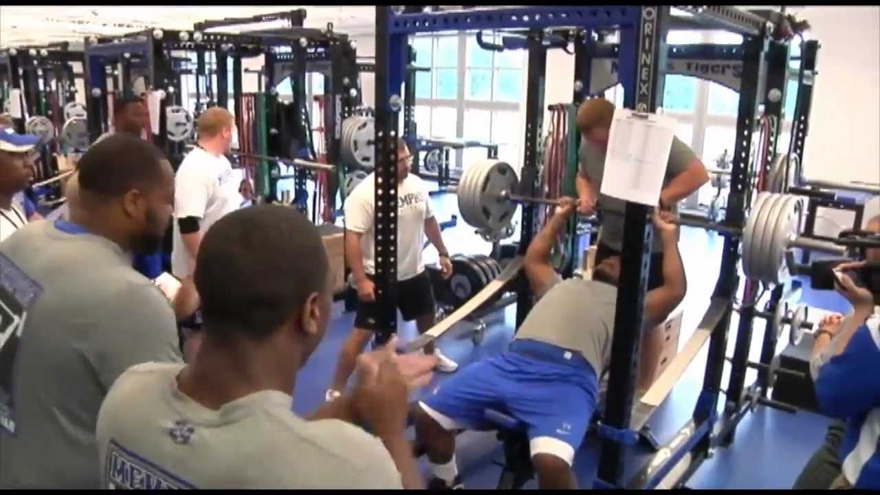 A lifter on a flat bench with shoulder blades retracted and chest lifted, holding a barbell at arm's length while a spotter watches closely