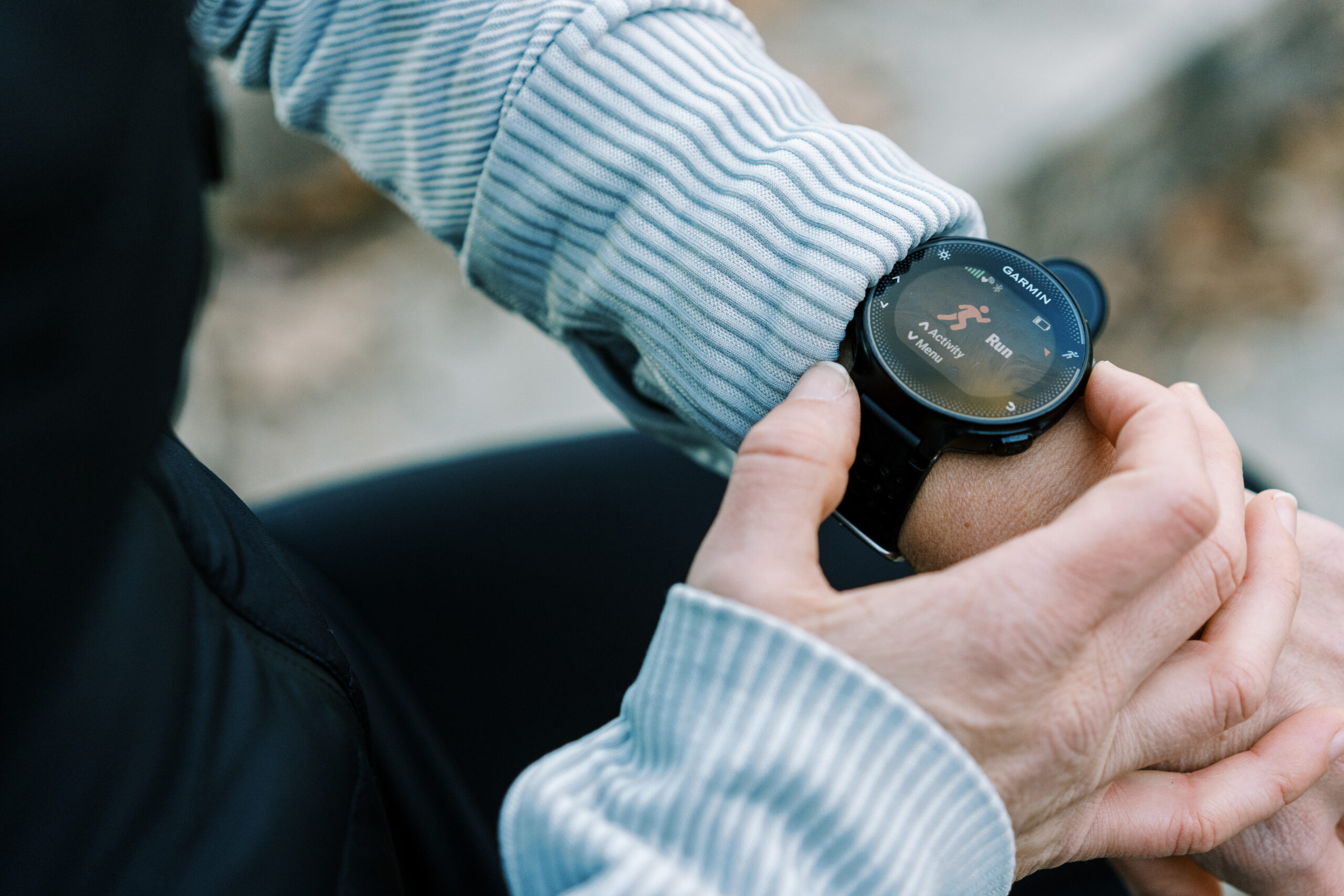 A marathon runner training in light rain wearing a GPS smartwatch, with water droplets visible on the watch face and wet pavement in the background