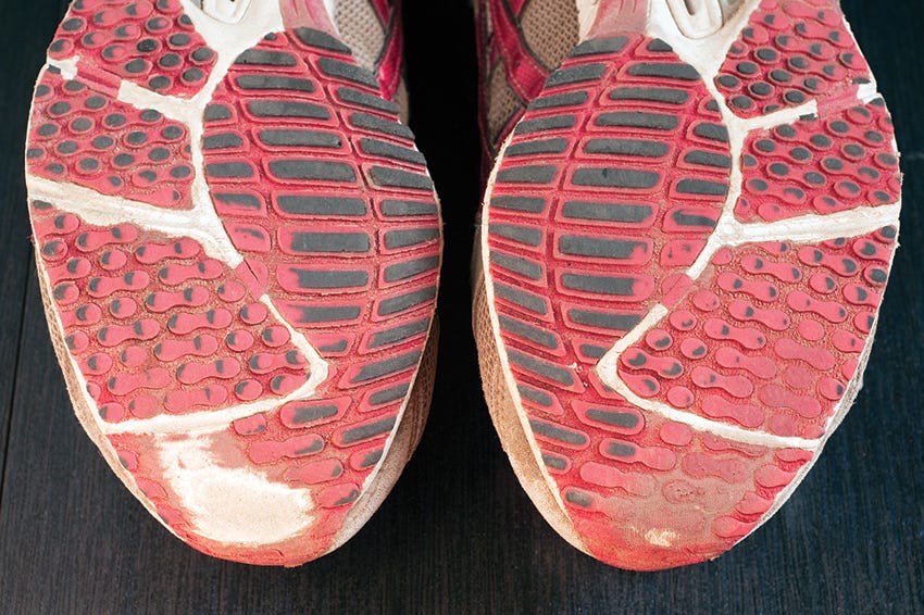 A pair of well-used road running shoes with visible outsole wear patterns, placed beside a water bottle near a track apron