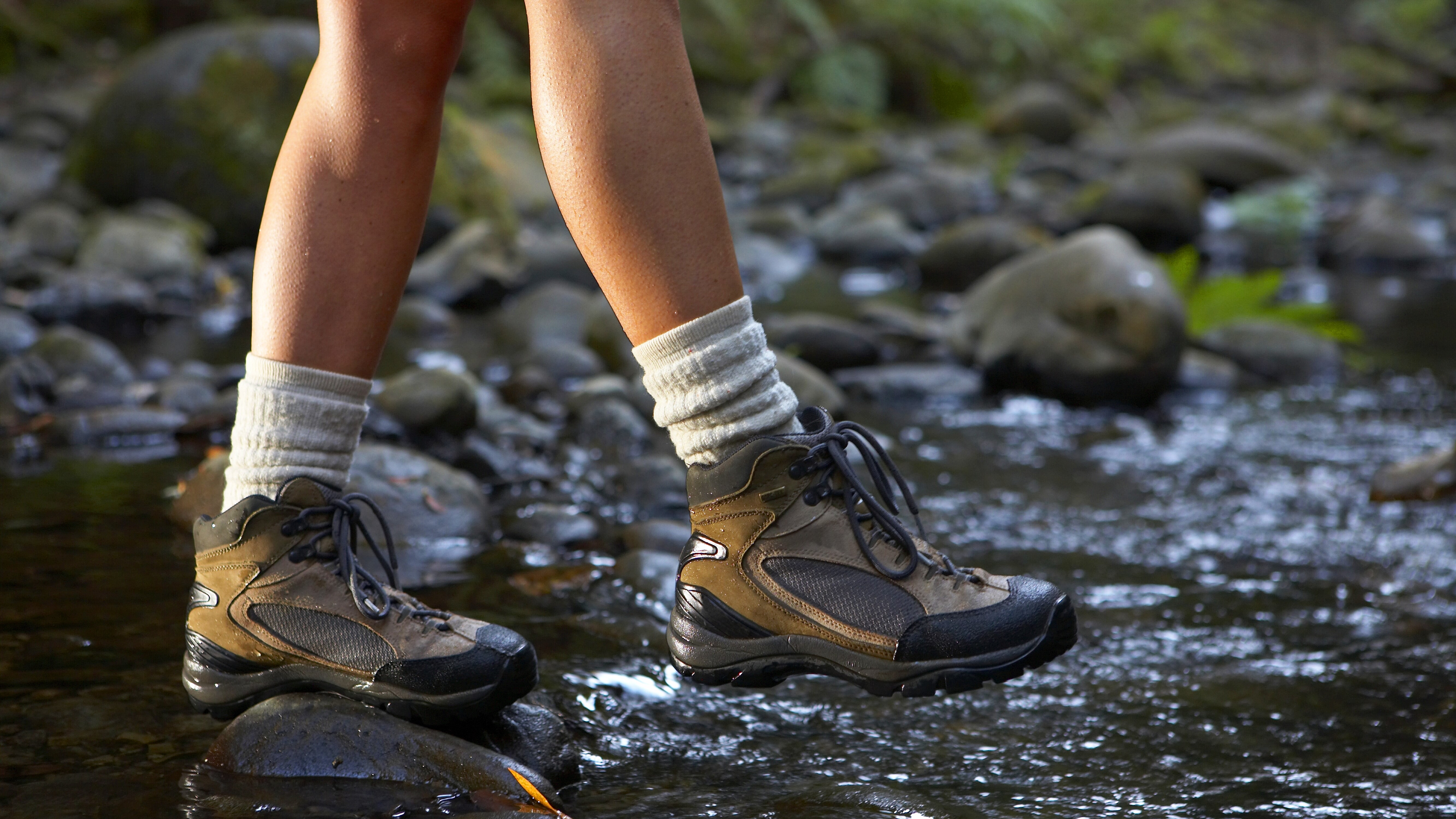 A person applying a spray-on waterproofing treatment to a synthetic hiking boot outdoors on a porch, with overspray visible in cold air
