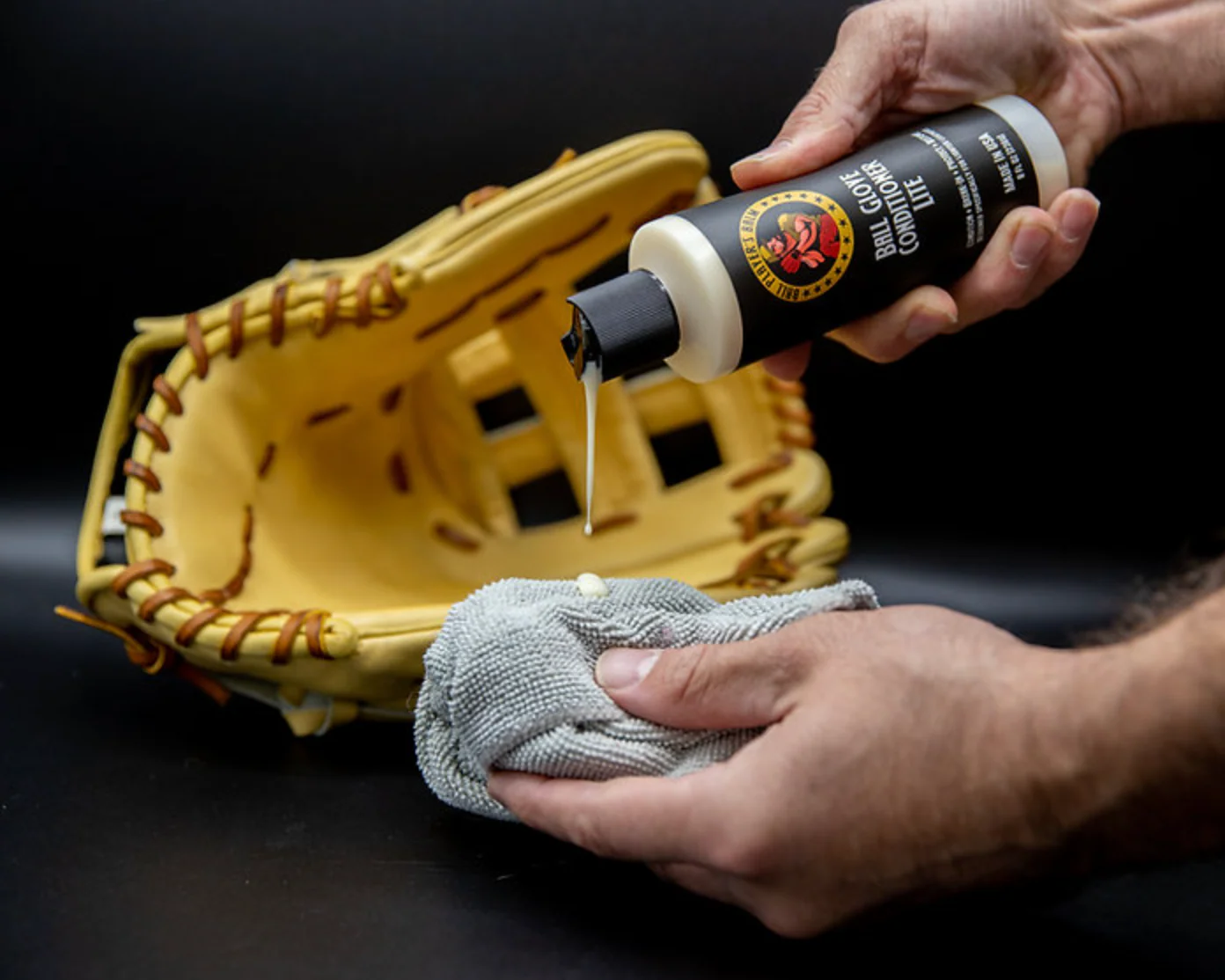 A player applying a small amount of leather conditioner to the palm of a baseball glove with a microfiber cloth in a locker room