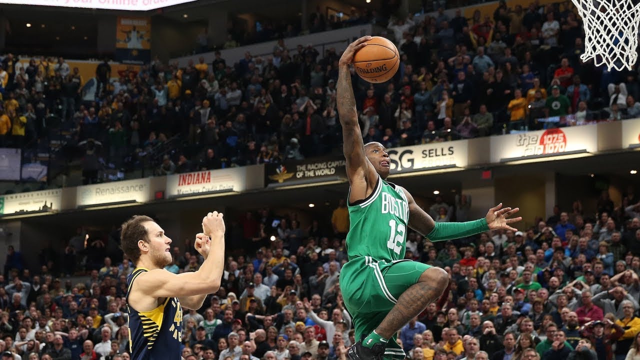 A player finishing a fast break dunk with two defenders trailing as the crowd rises behind the basket