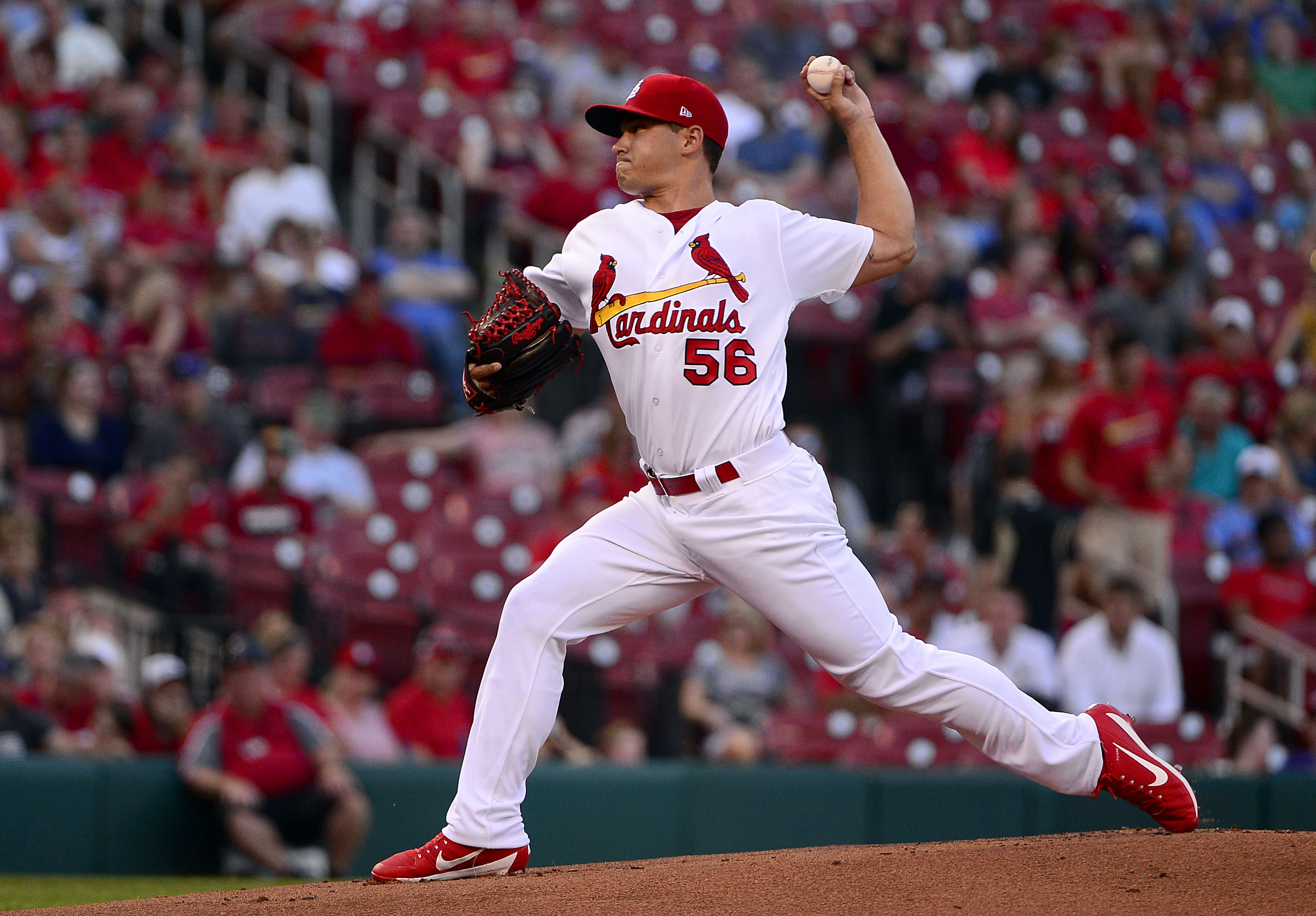 A professional baseball pitcher standing on the mound set to deliver a pitch, with the catcher crouched behind home plate and infielders ready
