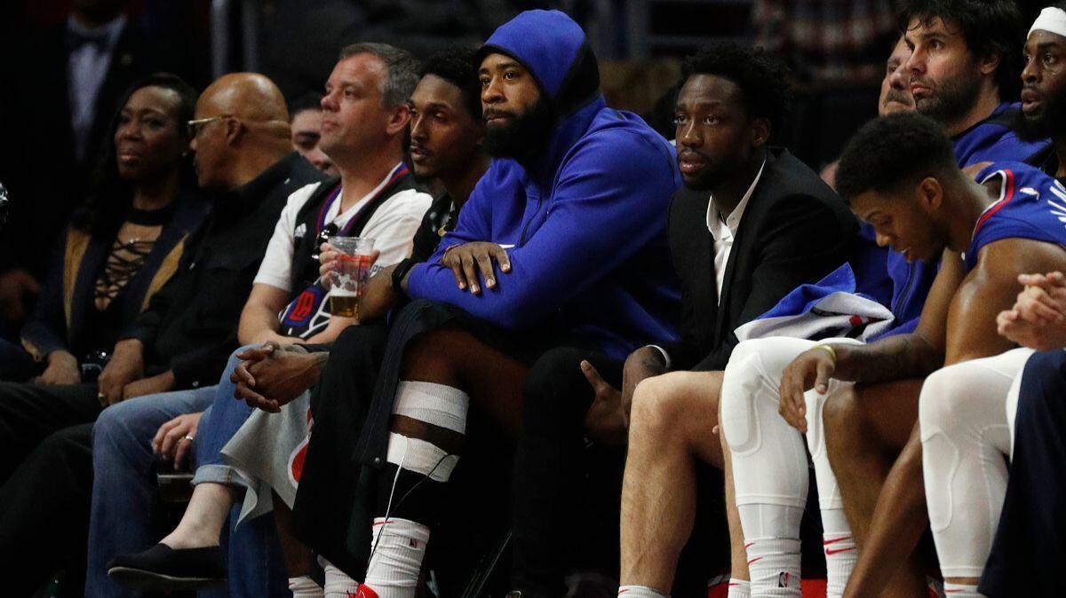 A professional basketball player sitting on the bench with his shoe off while a trainer checks his ankle as teammates watch during a tense game moment