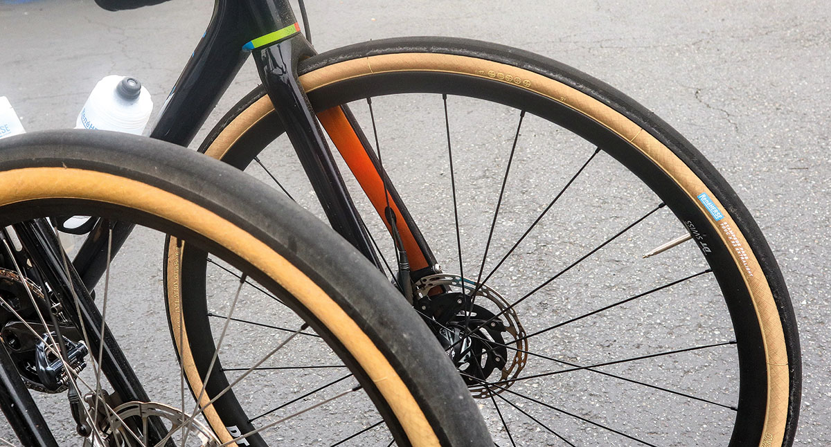 A road bike front wheel with a wide tire rolling over rough asphalt