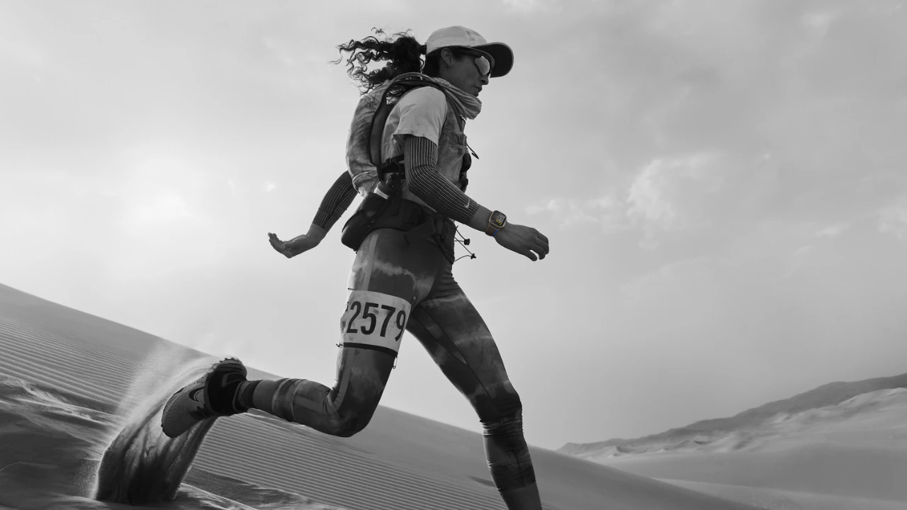 A runner doing a tempo workout on a track while wearing an Apple Watch Ultra, with lane markings visible and a focused mid-run posture