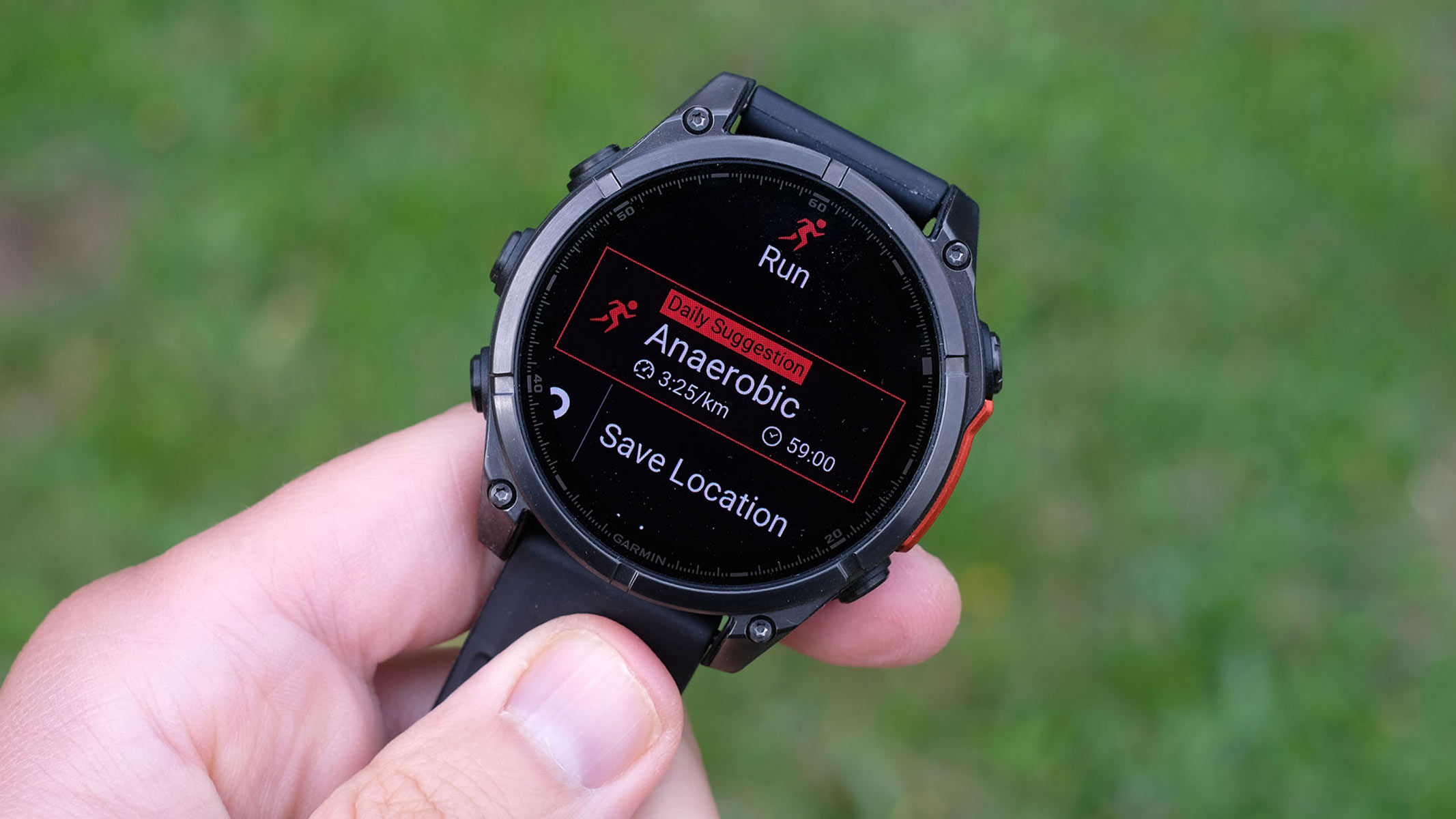 A runner on an outdoor track glancing down at a wristwatch displaying heart rate during training, late afternoon natural light
