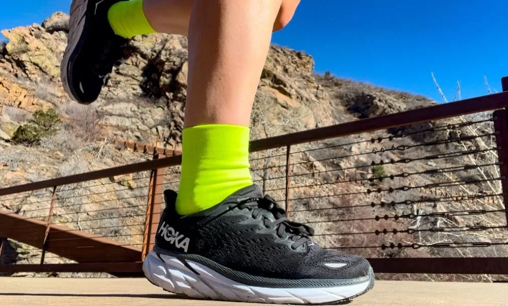A runner tying cushioned road running shoes while sitting on a park bench before a workout.