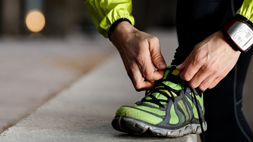 A runner tying the laces on a pair of cushioned running shoes on a sidewalk before a workout