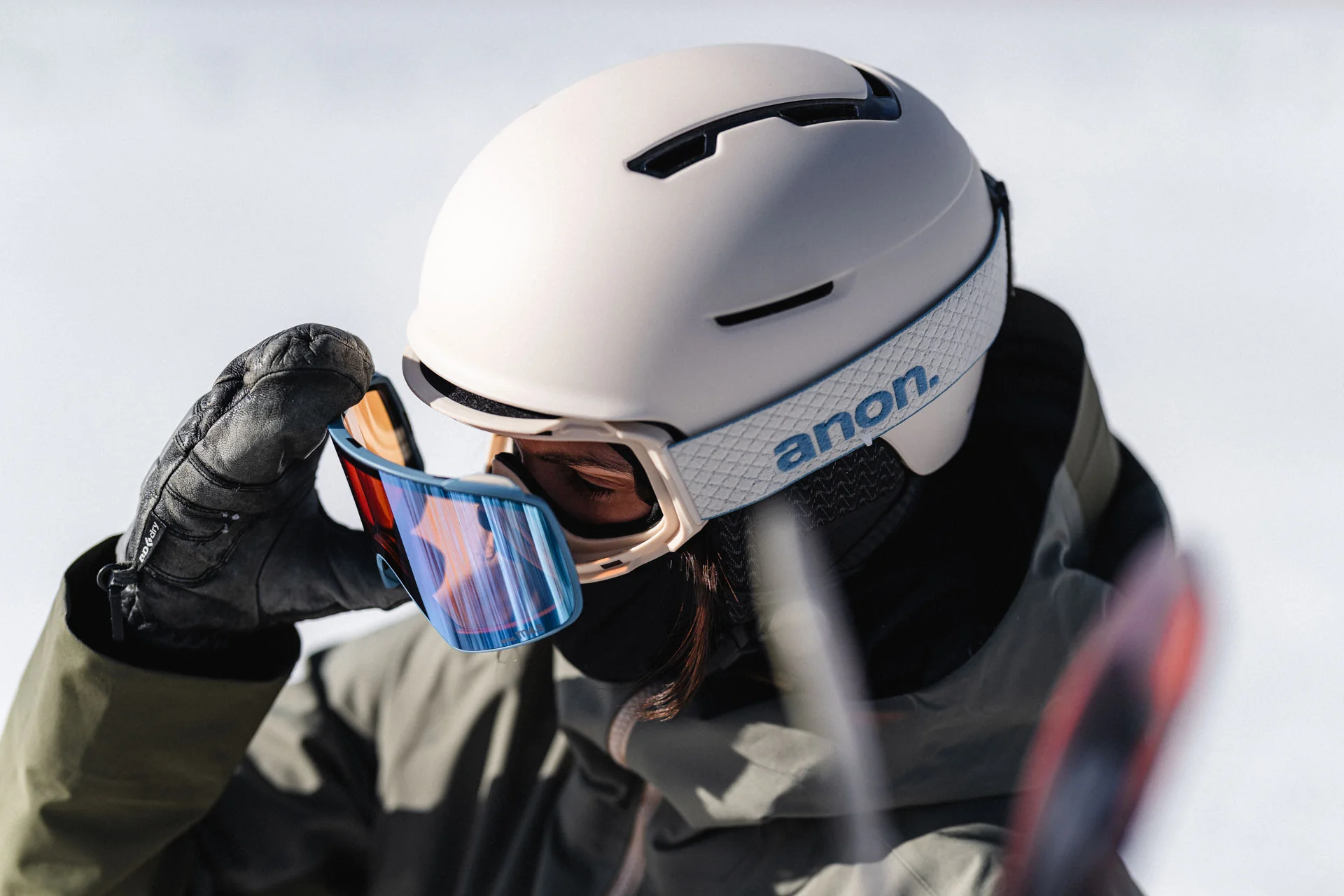 A skier wearing a properly fitted helmet and goggles with no forehead gap, standing outdoors near a chairlift