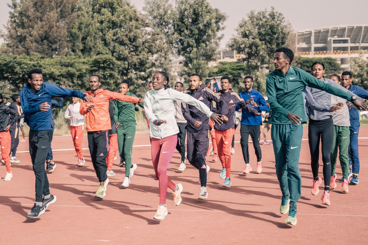 A small group of runners doing calf stretches along the edge of an outdoor track before a workout.