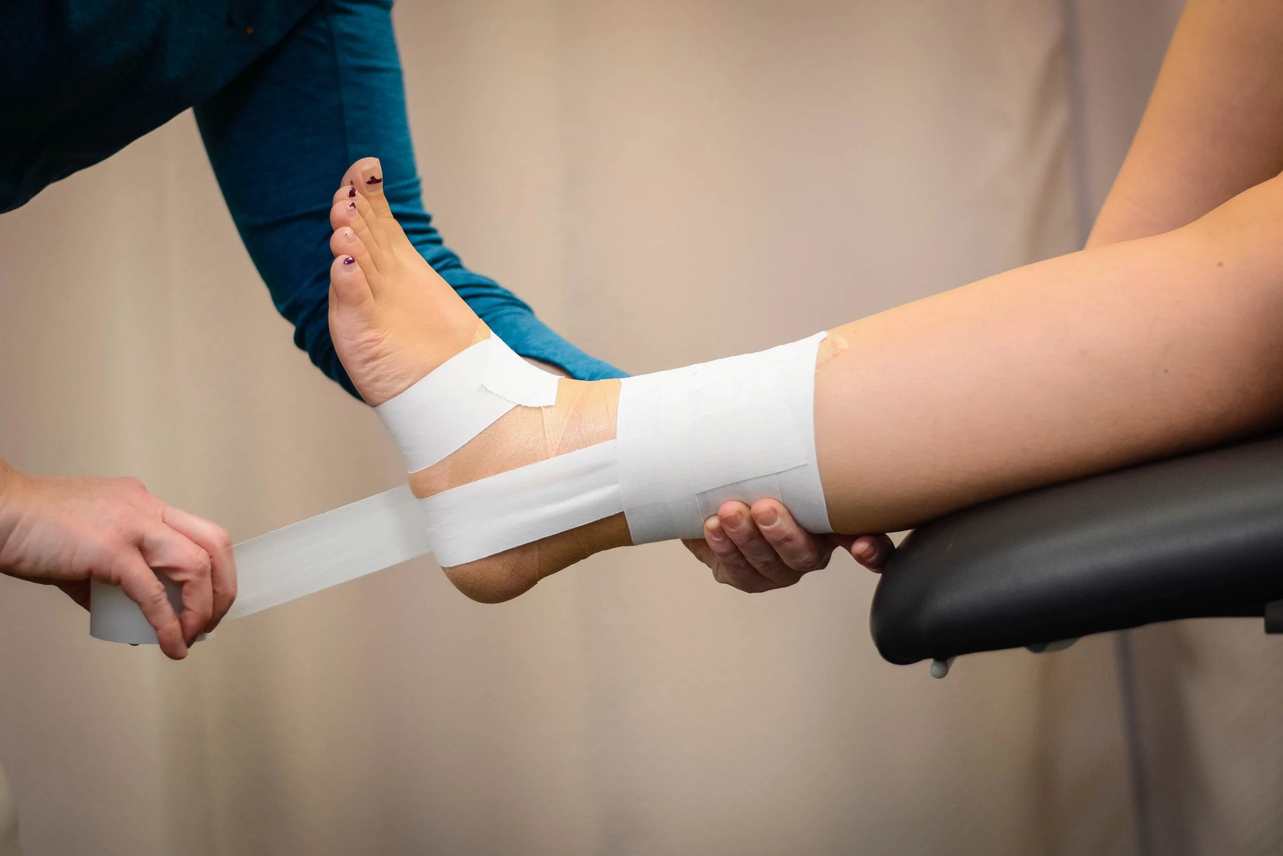 A sports athletic trainer applying white athletic tape to a player’s ankle in a locker room before a game