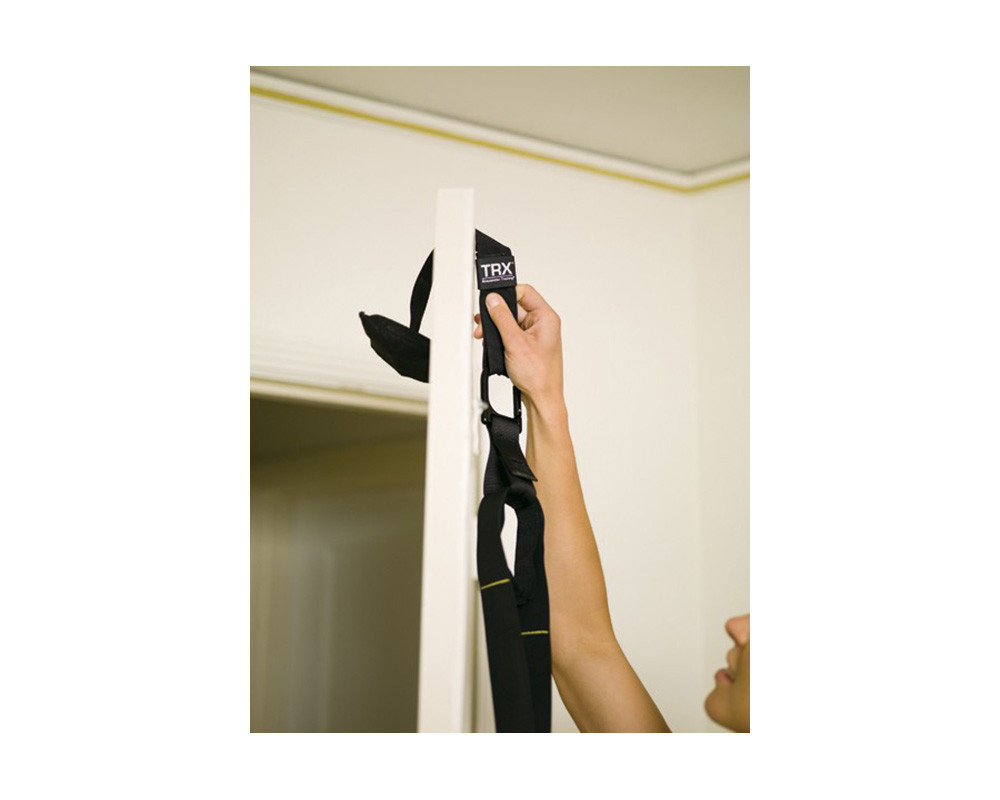A suspension trainer anchored over a sturdy door with a person setting up for bodyweight rows in a small apartment
