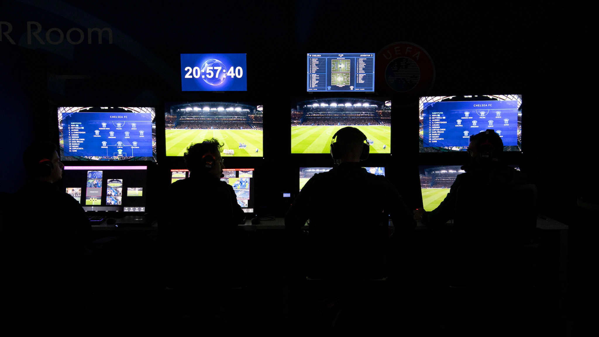 A team of video assistant referees sitting in a control room monitoring multiple live camera angles during a major European match