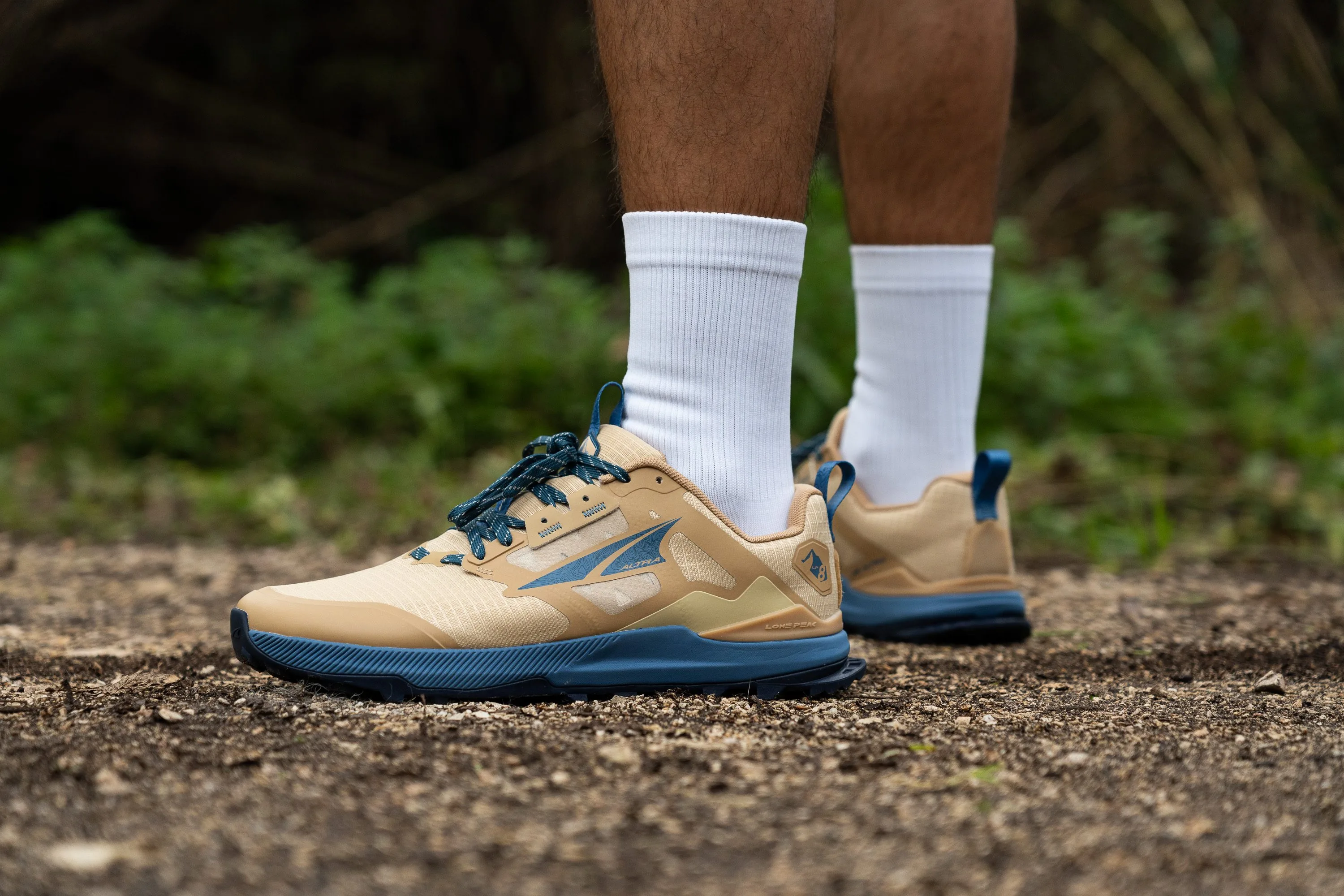An Altra Lone Peak 8 trail shoe on packed dirt with pine needles, highlighting a roomy toe box and low drop profile