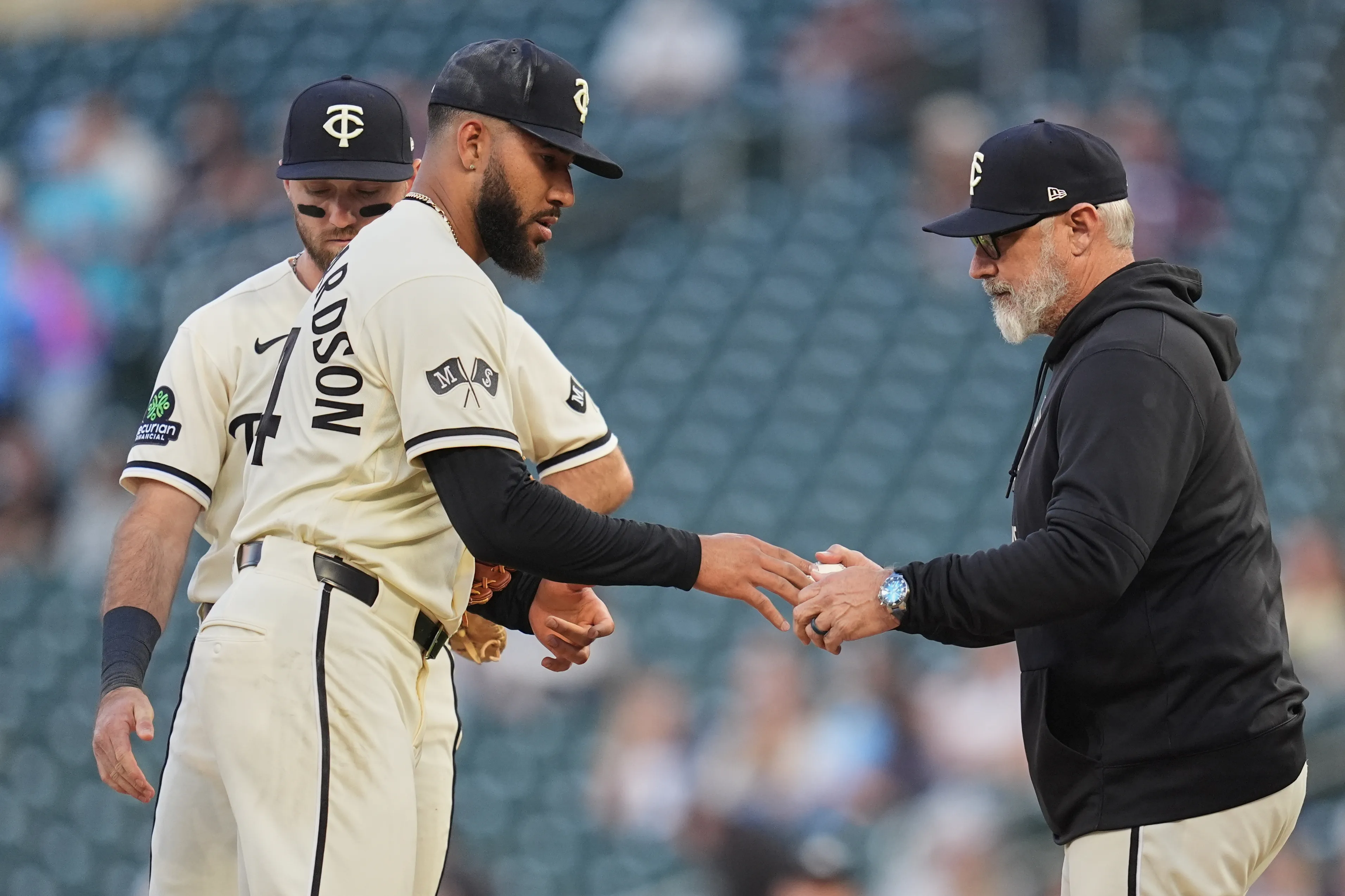 An MLB manager walking to the mound to make a pitching change while players watch from the infield during a live game