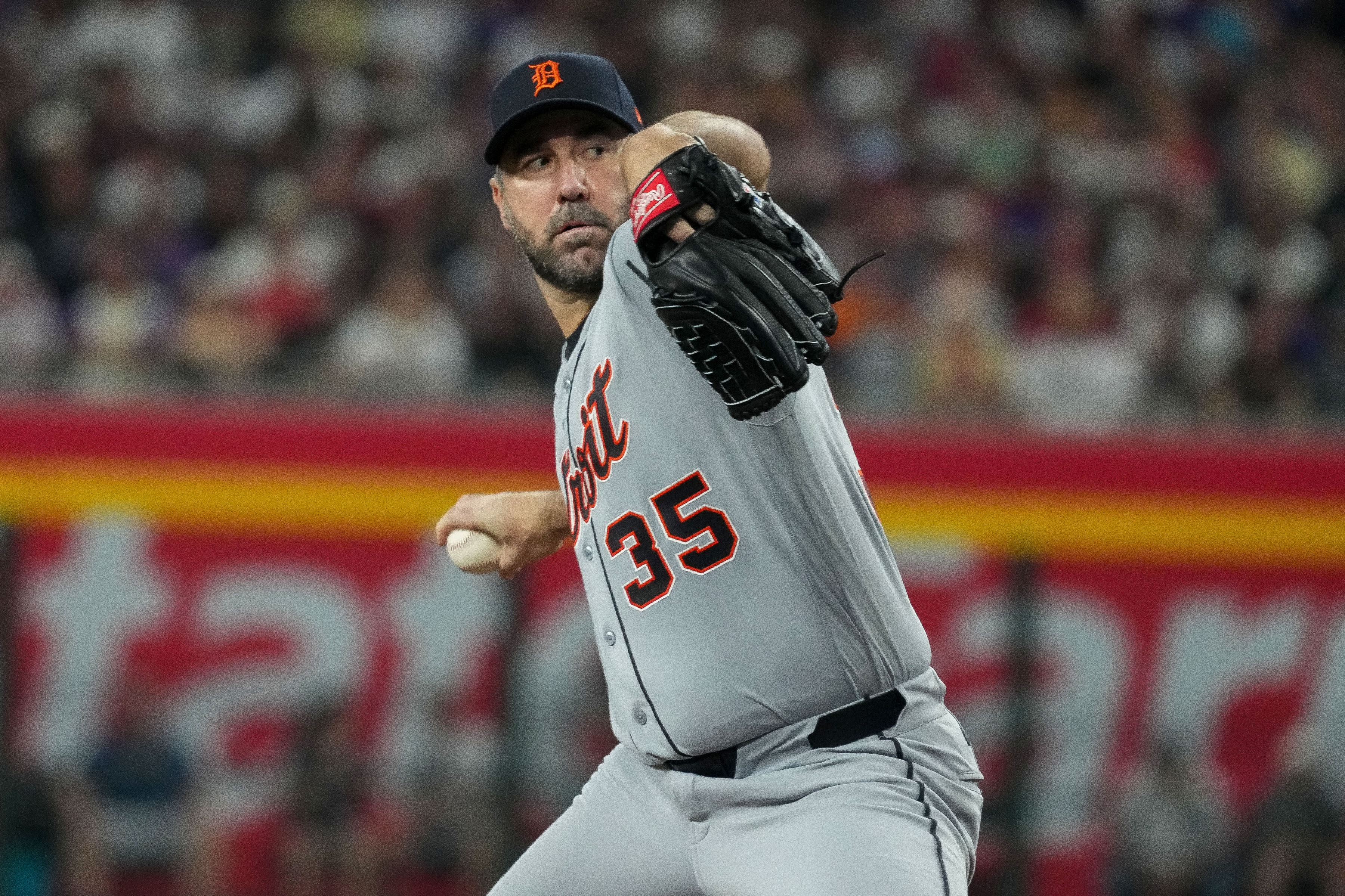 An MLB pitcher doing a rehabilitation throwing session on a side field while a trainer observes, with nets and bullpen mounds nearby