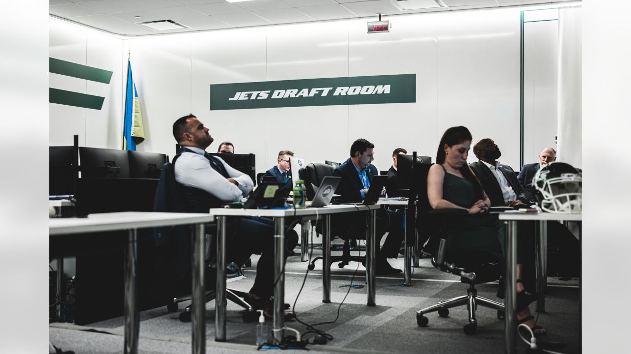 An NFL team draft room scene in 2024 with a general manager and staff seated at a table, laptops open, and team branding visible on apparel