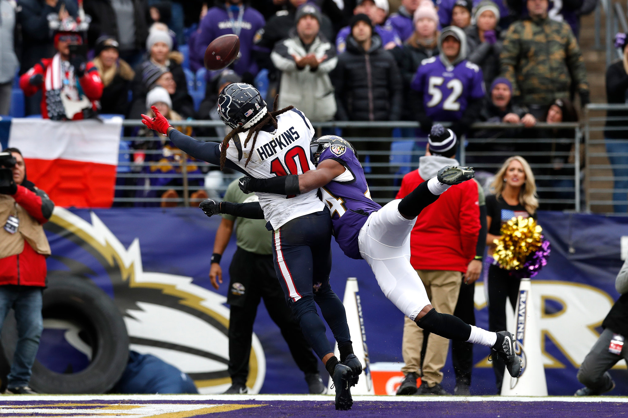 An NFL wide receiver and defensive back fighting for position as a deep pass drops in over their shoulders near the sideline, game action photograph