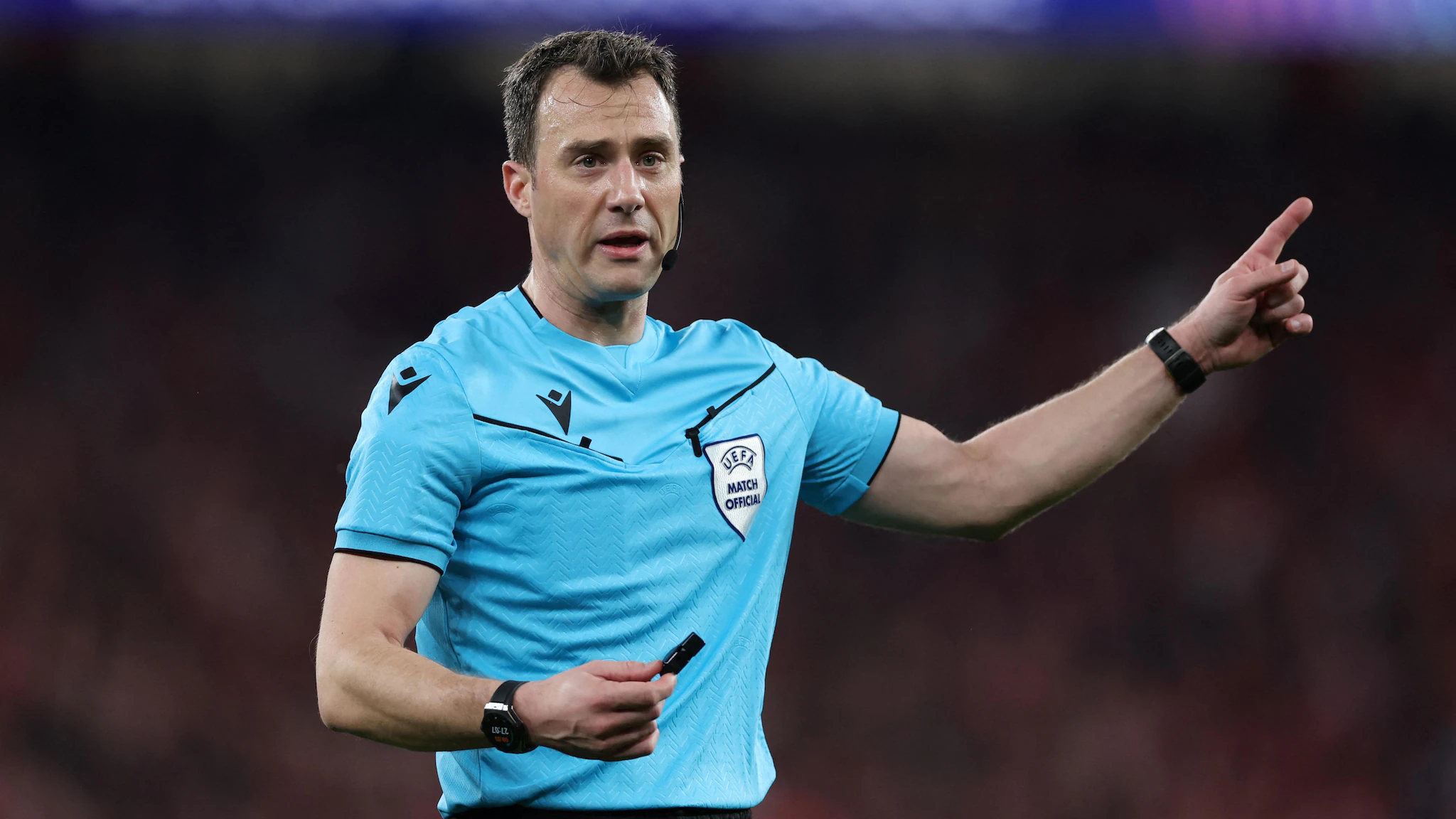 An assistant referee on the sideline raising a flag to signal an offside call during a professional soccer match in a large stadium