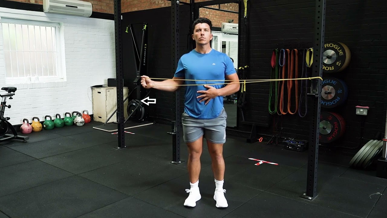An athlete in a gym performing a banded external rotation exercise with the elbow tucked at the side, focusing on shoulder stability