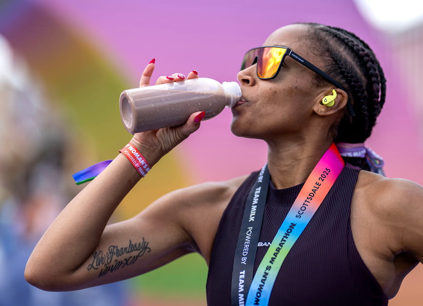 An athlete in training clothes holding a bottle of chocolate milk outside a gym entrance
