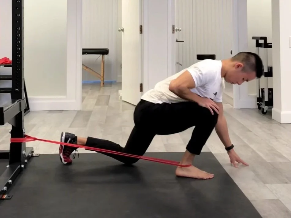 An athlete performing a banded ankle mobility stretch near a squat rack, with the band anchored low