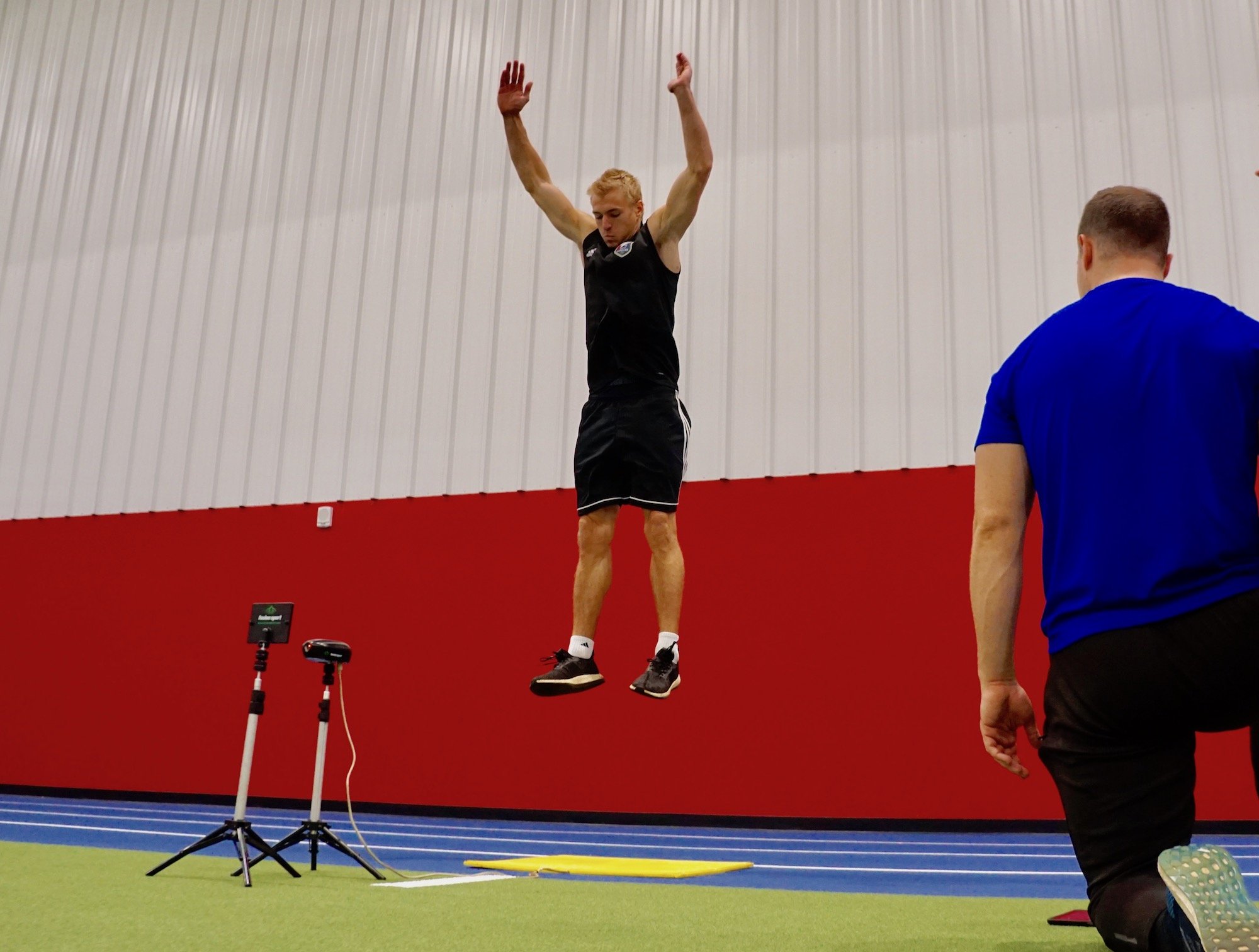 An athlete reaching up to touch a high mark on a wall during a vertical jump test in a gym, real photo