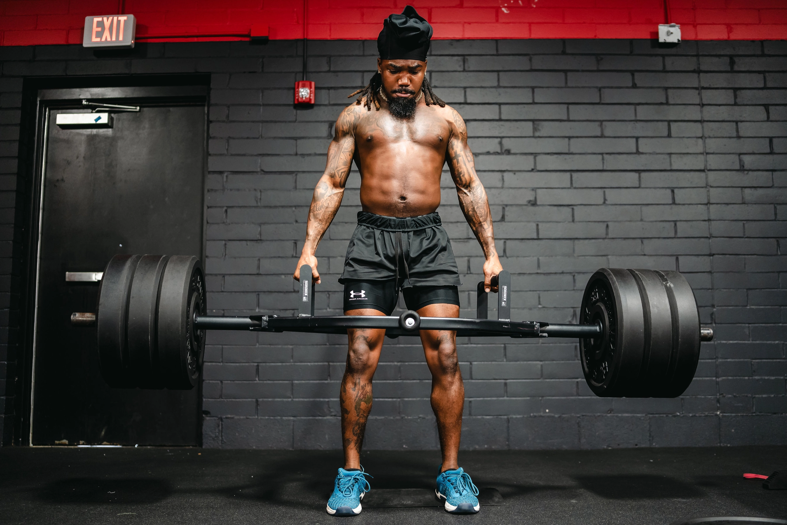 An athlete setting up for a deadlift with a loaded barbell on a gym platform, hips back and back flat, preparing to lift