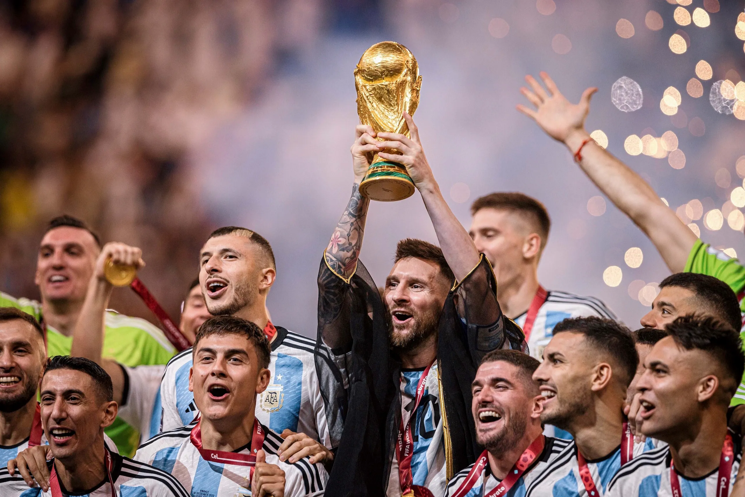 Argentina players celebrating together on the field after winning the 2022 World Cup final with fans waving flags in the stands