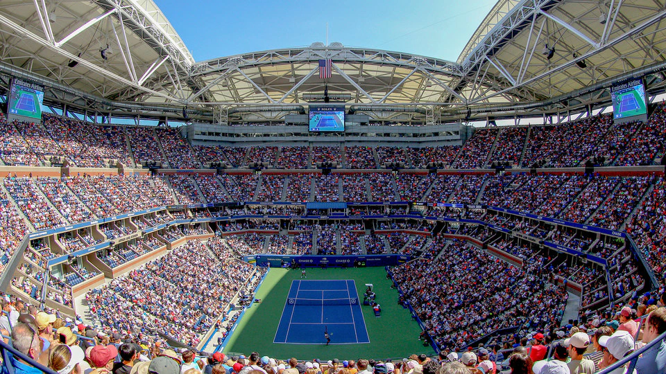 Arthur Ashe Stadium at the USTA Billie Jean King National Tennis Center on a sunny day, with the court visible inside.
