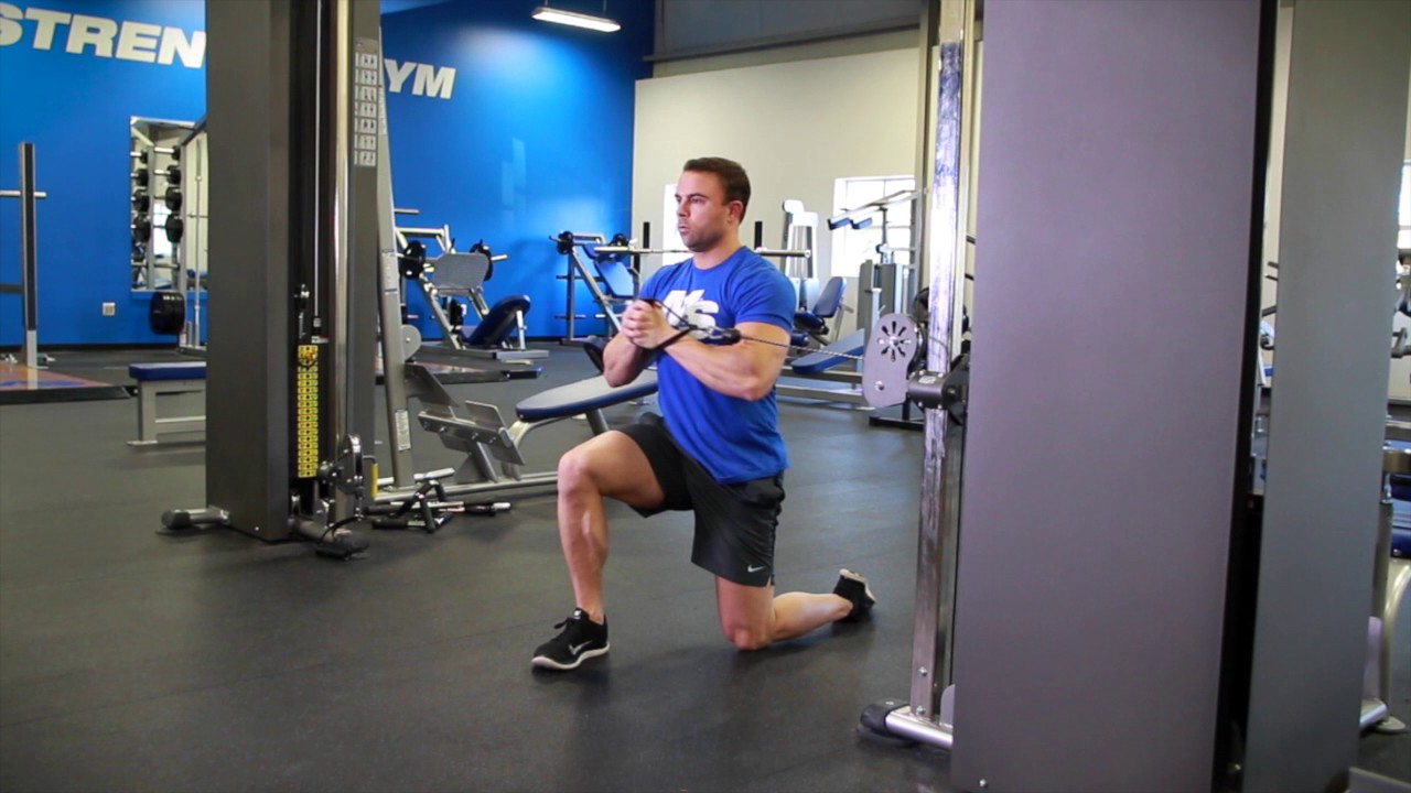 Athlete performing a half-kneeling Pallof press with a resistance band anchored to a rack, maintaining a tall posture