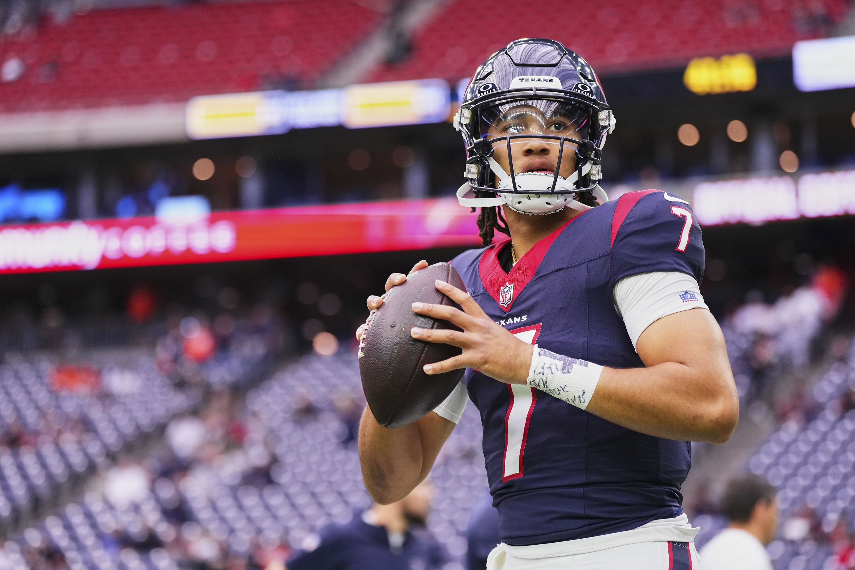 C.J. Stroud in a Houston Texans uniform dropping back to pass, scanning downfield with linemen engaged at the line of scrimmage