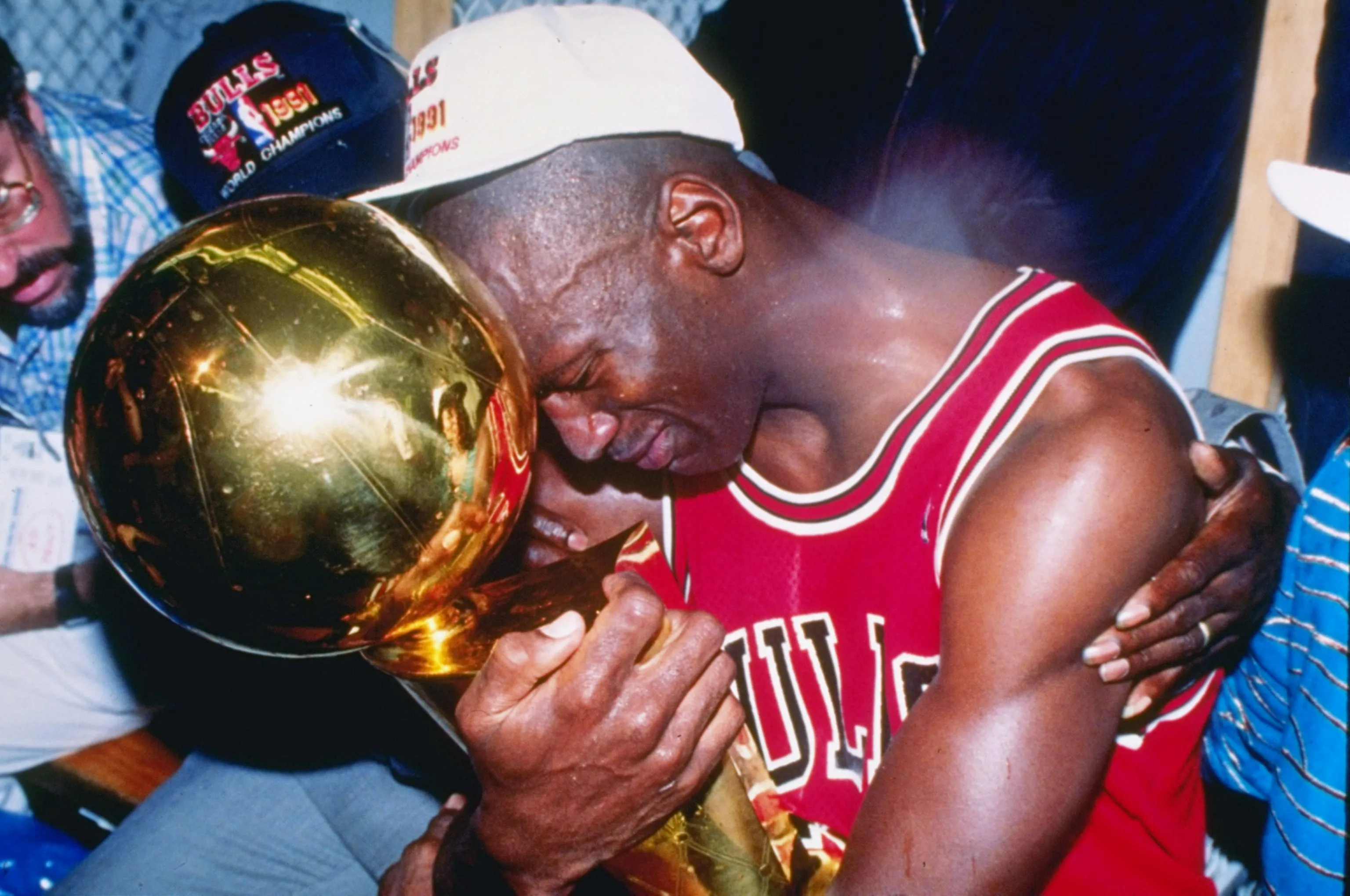 Chicago Bulls players celebrating on the court after winning the NBA Finals, with teammates clustered together and confetti beginning to fall from the arena rafters