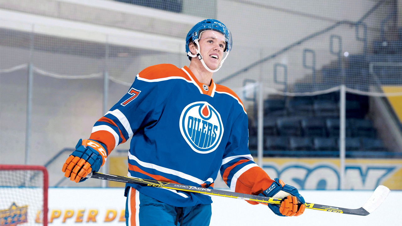 Connor McDavid skating at speed through the neutral zone with the puck as a defender angles him toward the boards