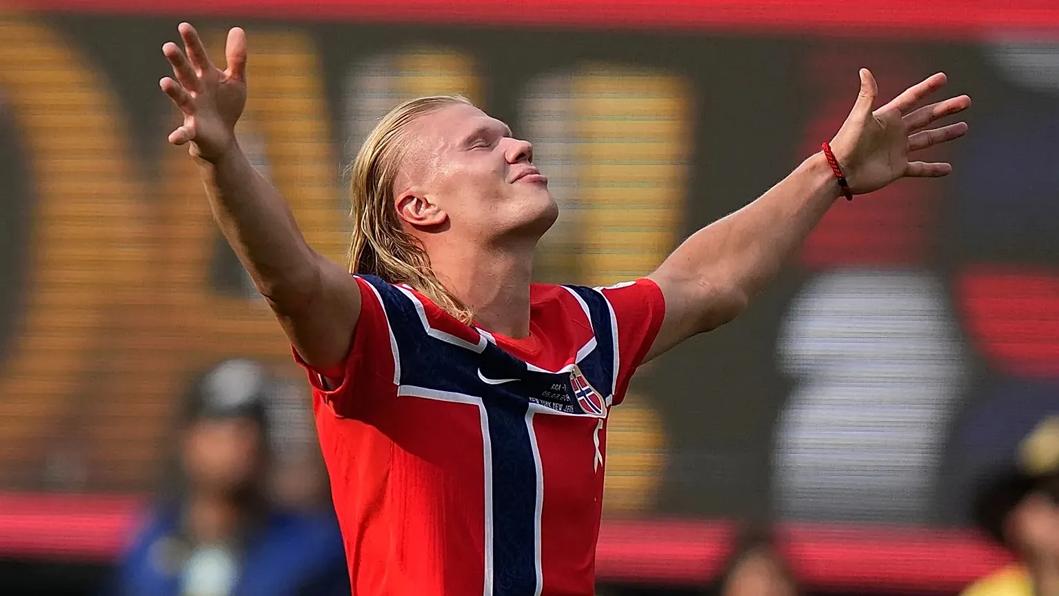 Erling Haaland in Norway kit celebrating a goal during a 2026 World Cup match, with teammates running toward him and fans blurred in the stands