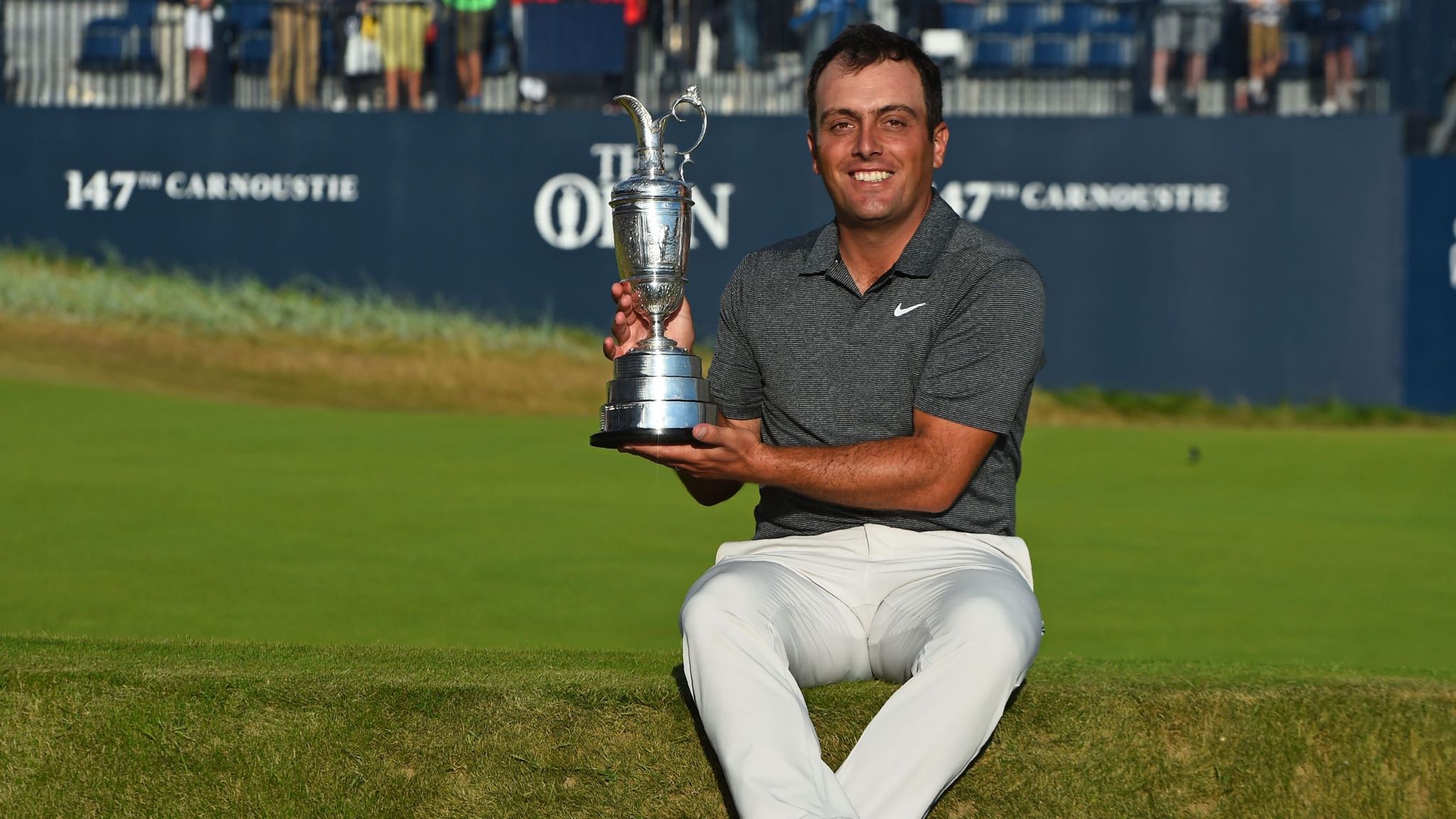 Francesco Molinari holding the Claret Jug on the 18th green at Carnoustie after winning The Open in 2018, surrounded by fans