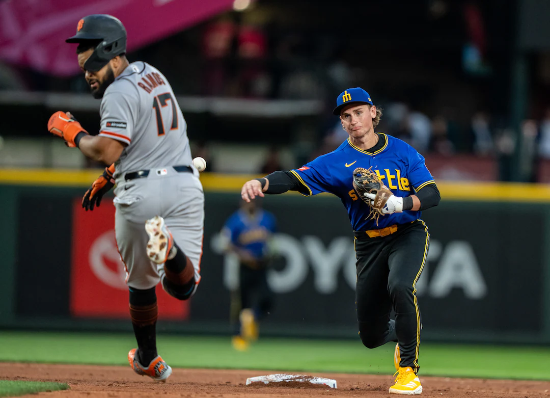 Game action during a San Francisco Giants vs. Seattle Mariners matchup, with a pitcher delivering a pitch as the batter loads and fans watch under stadium lights